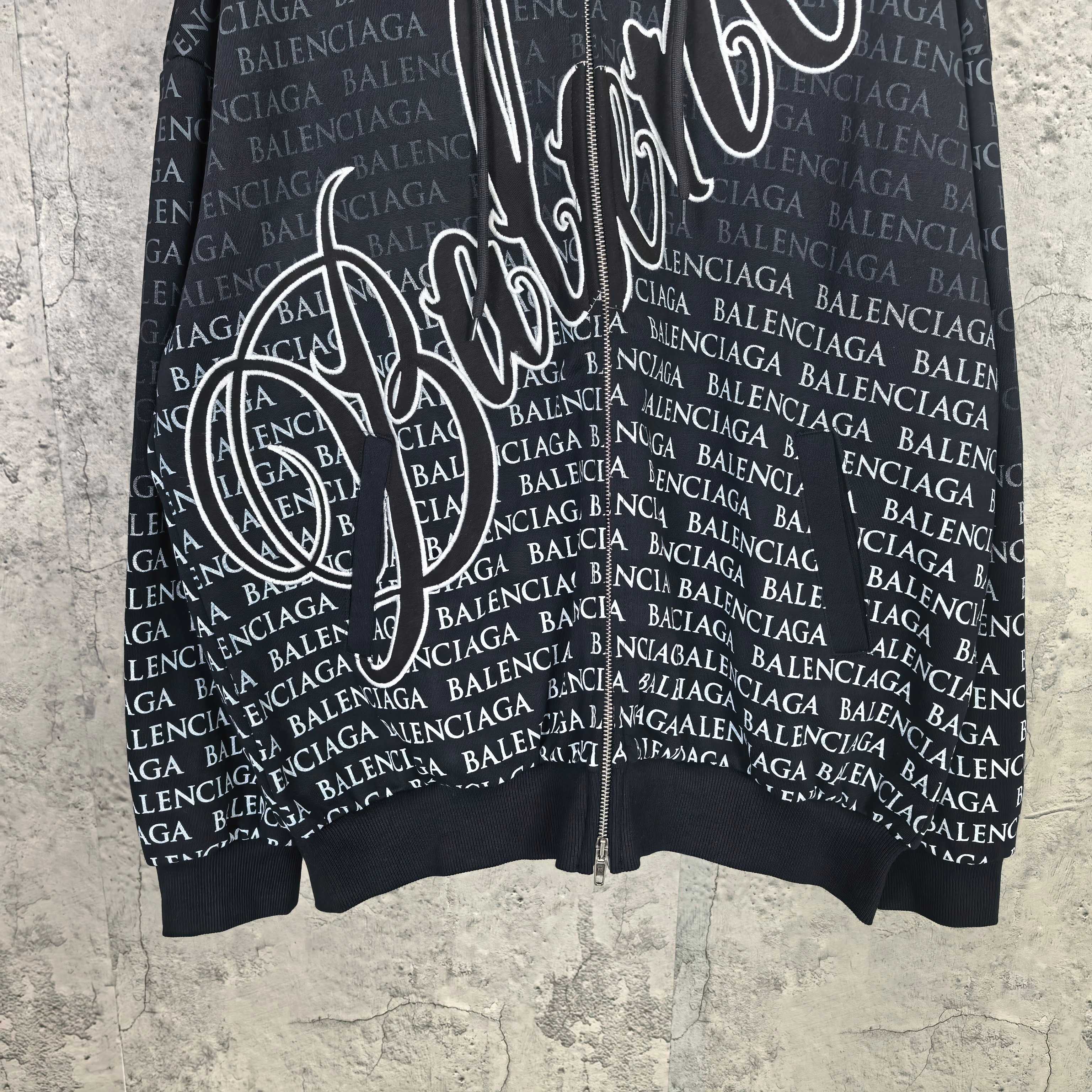 Front close-up of dark long-sleeve zip hoodie with allover Balenciaga text and graphic print.