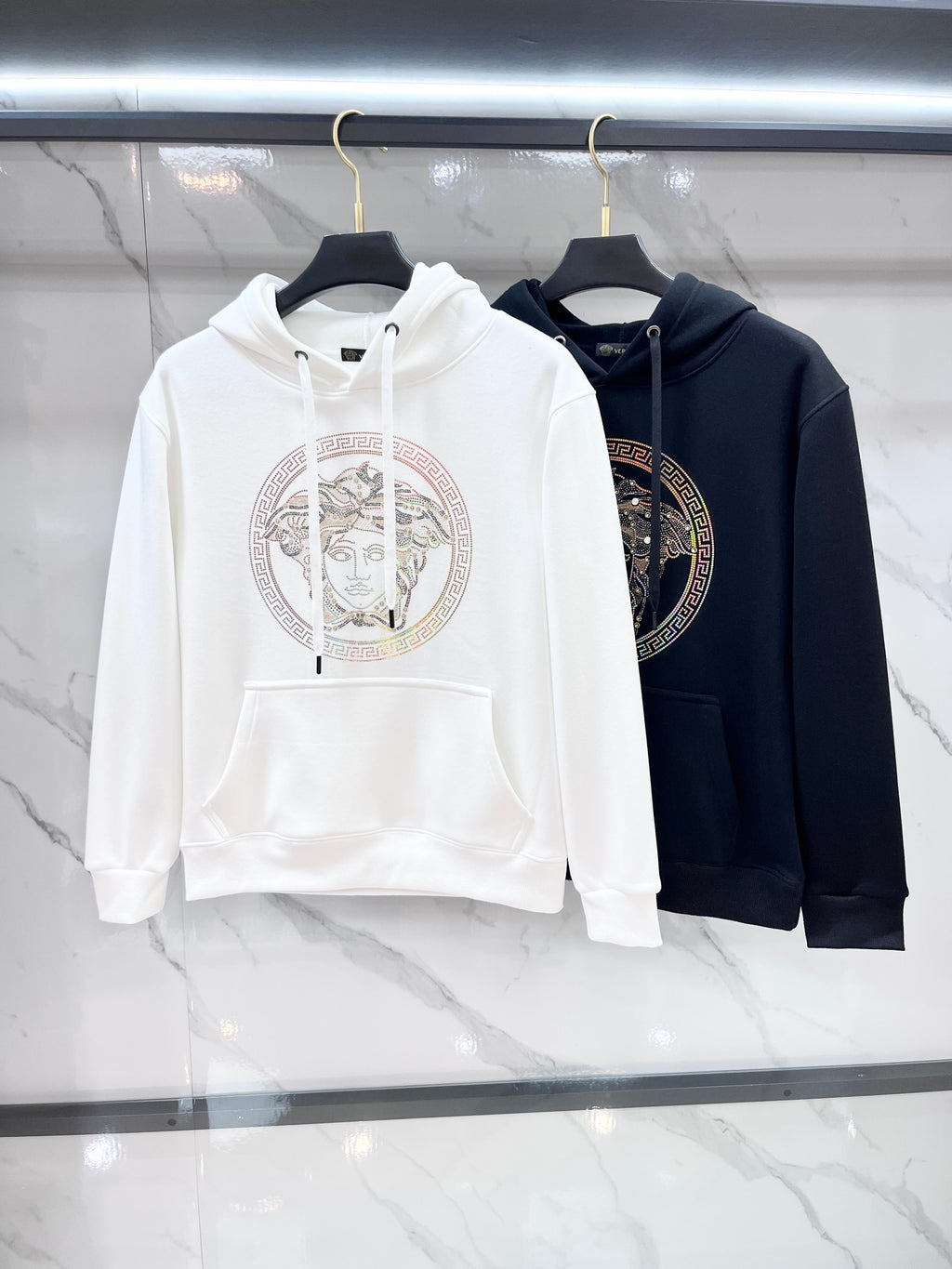 Pair of hooded sweatshirts: white and dark, each with circular Medusa rhinestone print