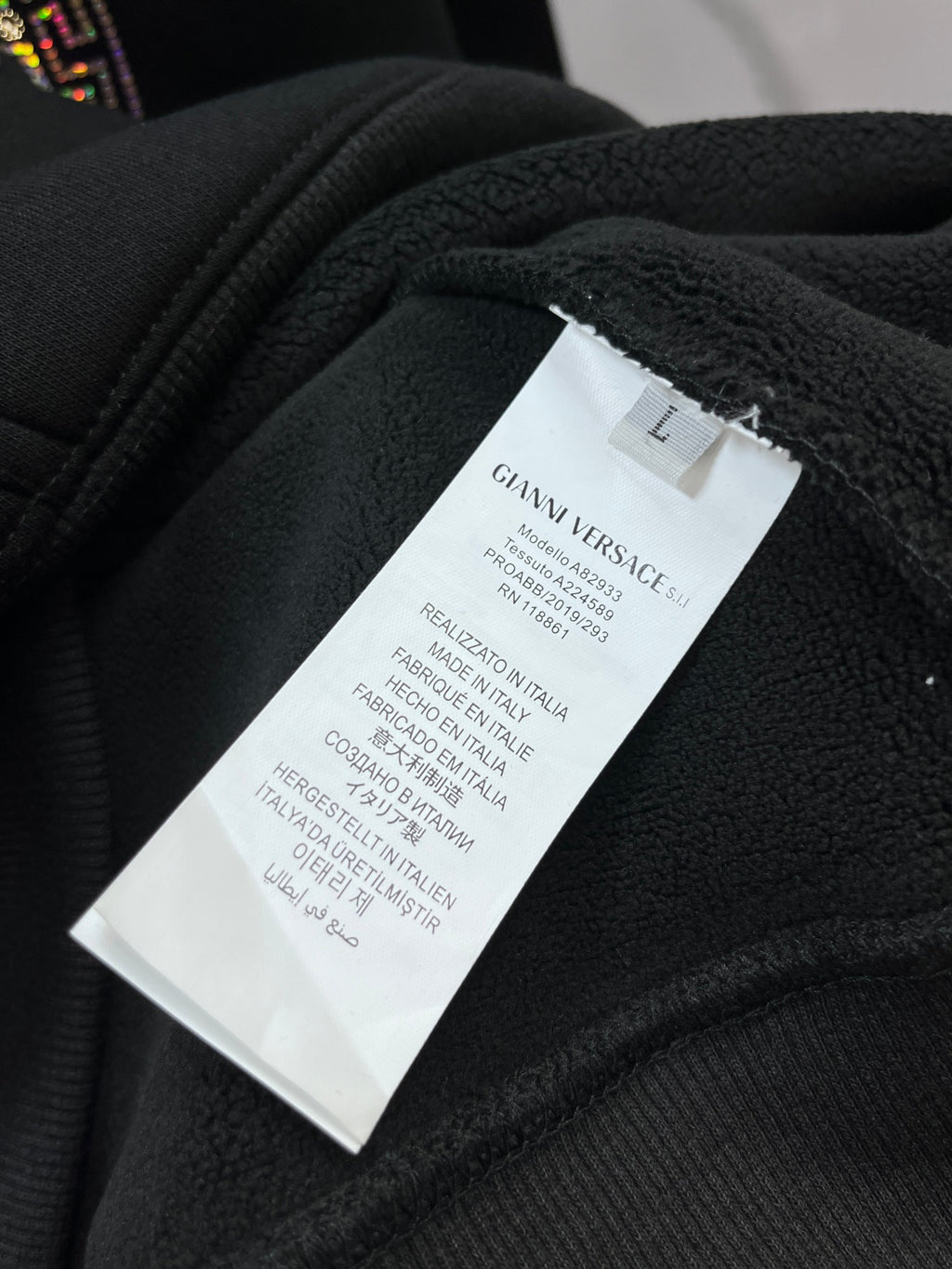 Clothing label reading GIANNI VERSACE and size L on dark hoodie fabric