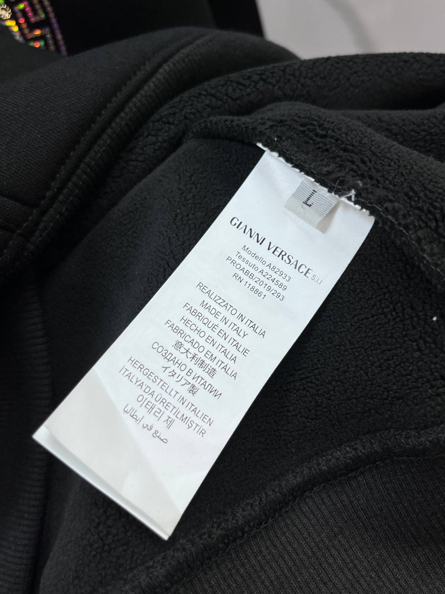 Clothing label reading GIANNI VERSACE and size L on dark hoodie fabric
