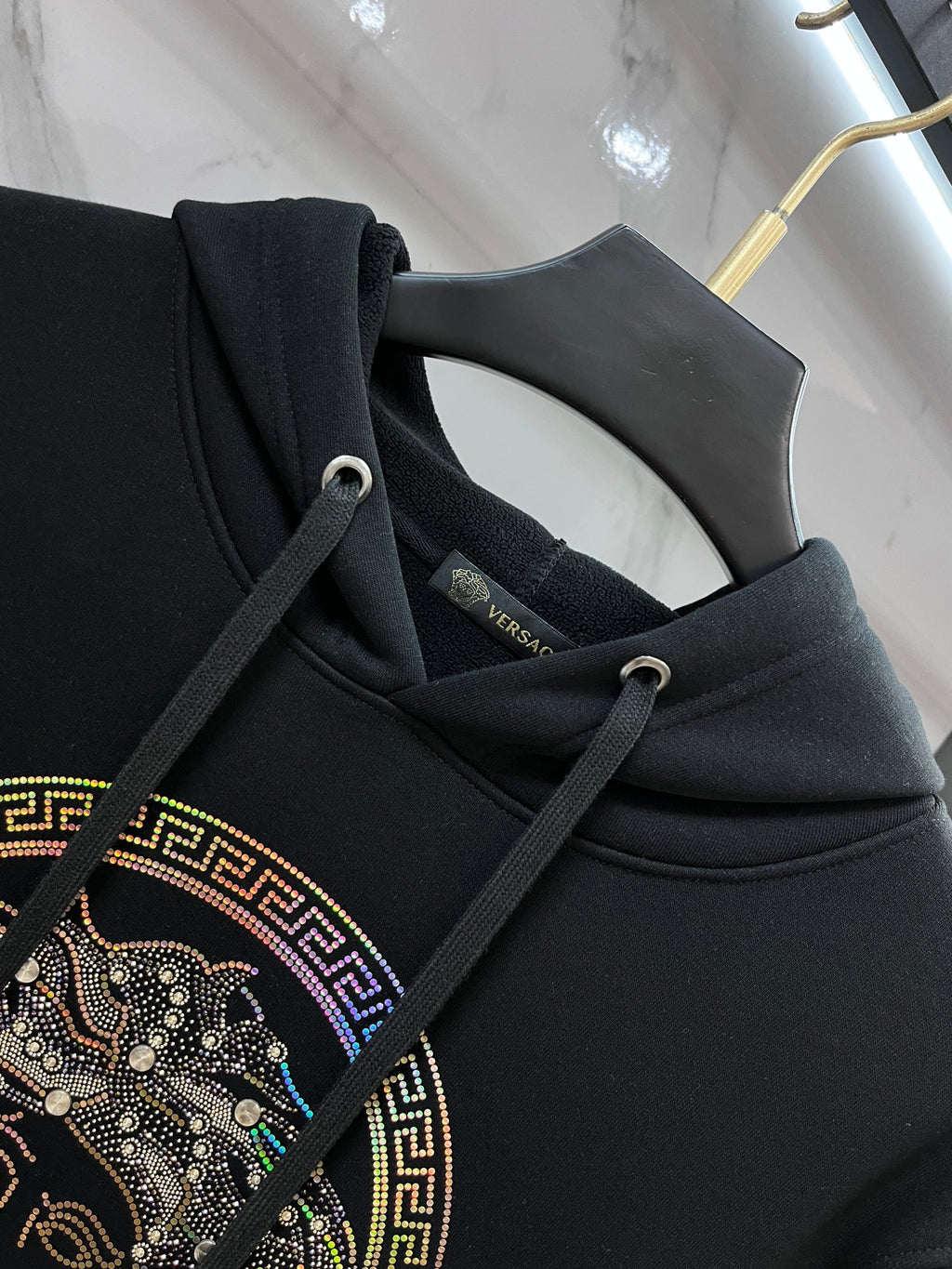 Dark hoodie neckline with drawstrings and rhinestone Medusa emblem on chest