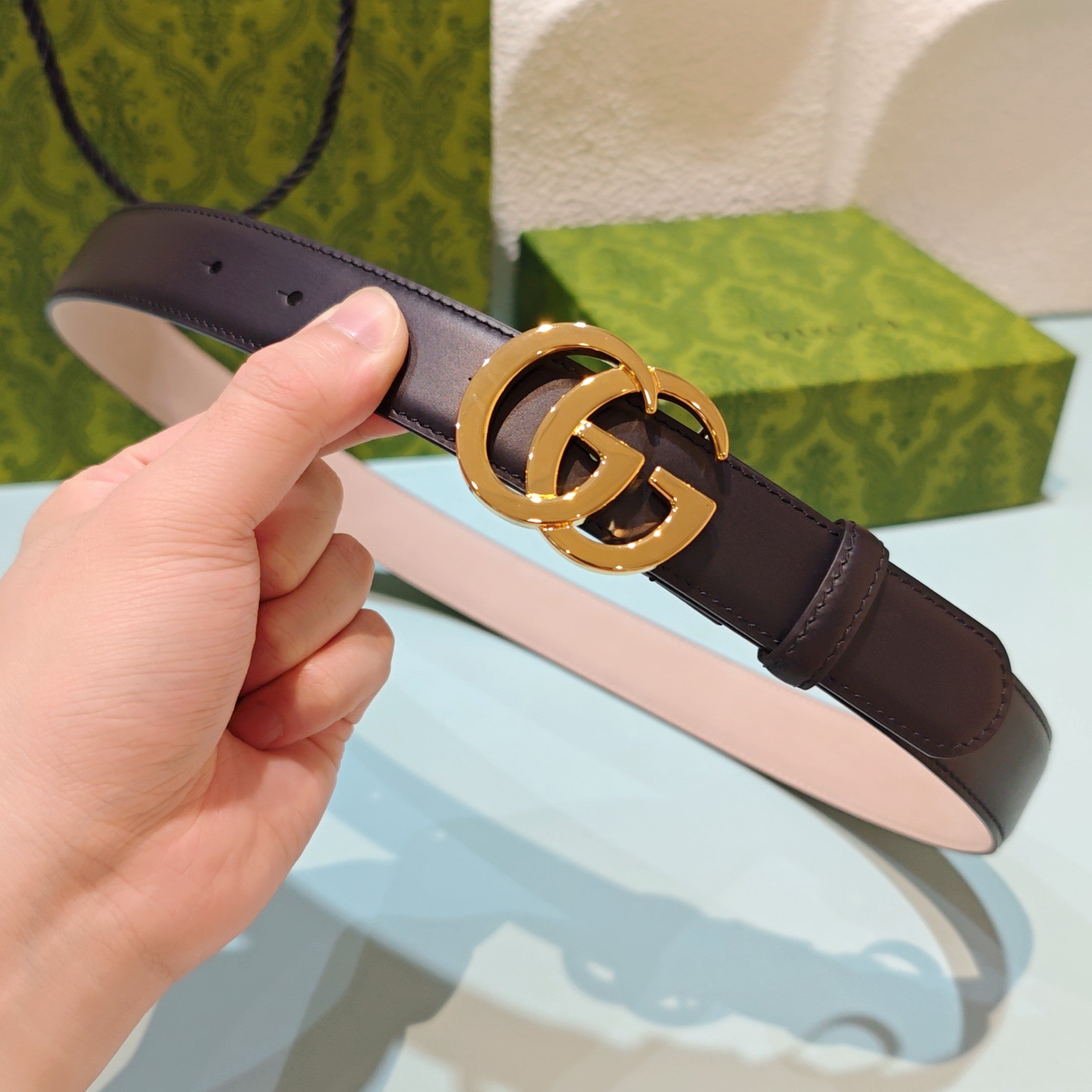 Gucci belt with dark leather strap and gold GG buckle, held in hand
