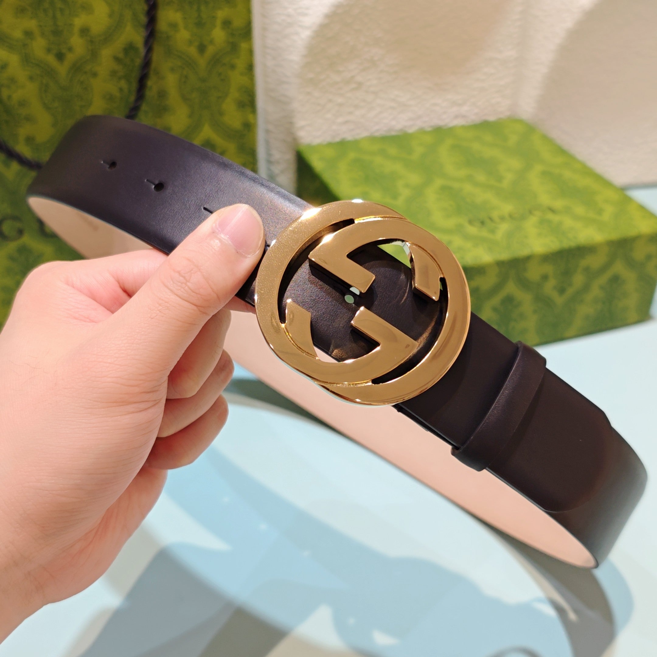 Gucci belt with dark leather strap and gold-tone GG logo buckle, close-up in hand