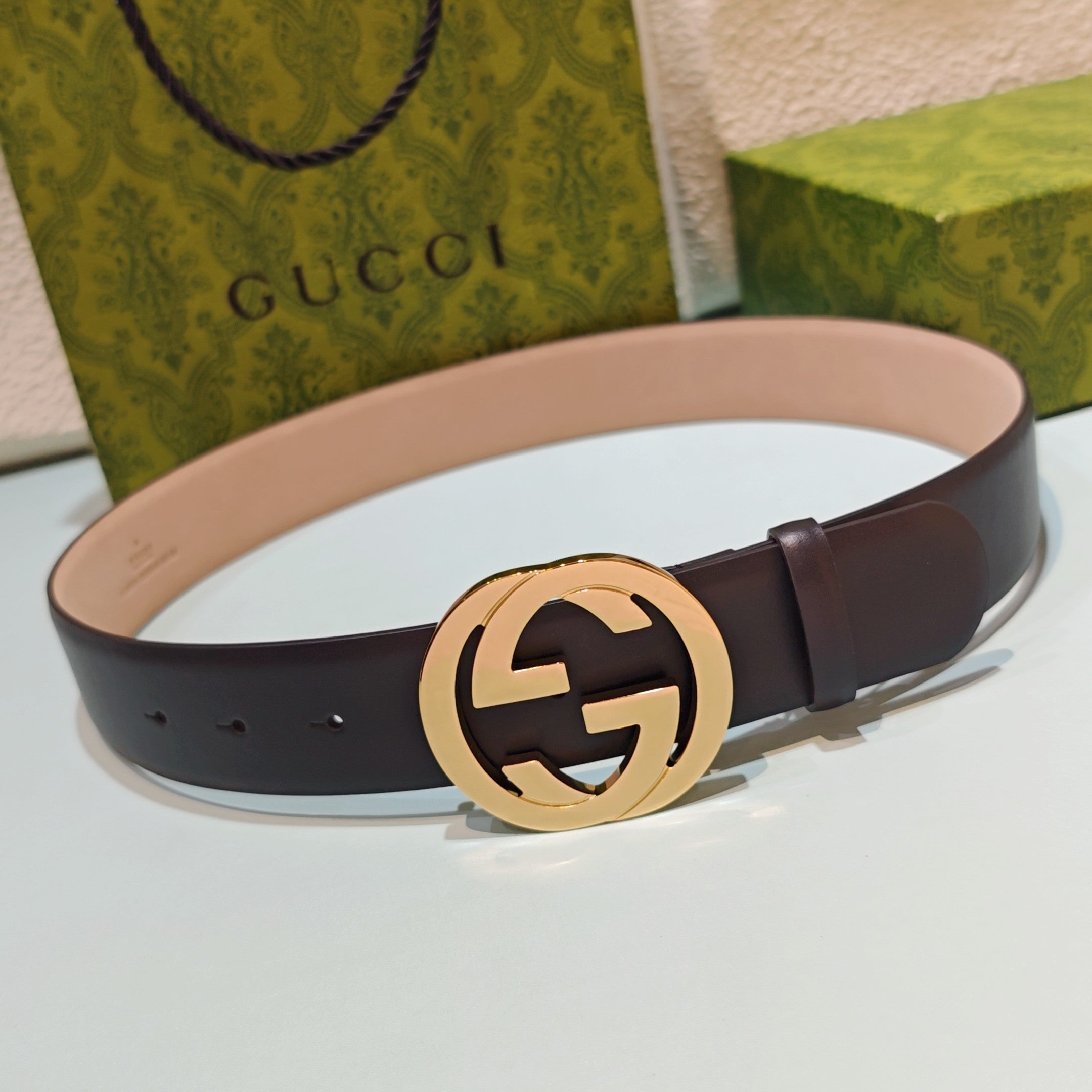 Dark leather belt with gold-tone round GG logo buckle on a smooth strap