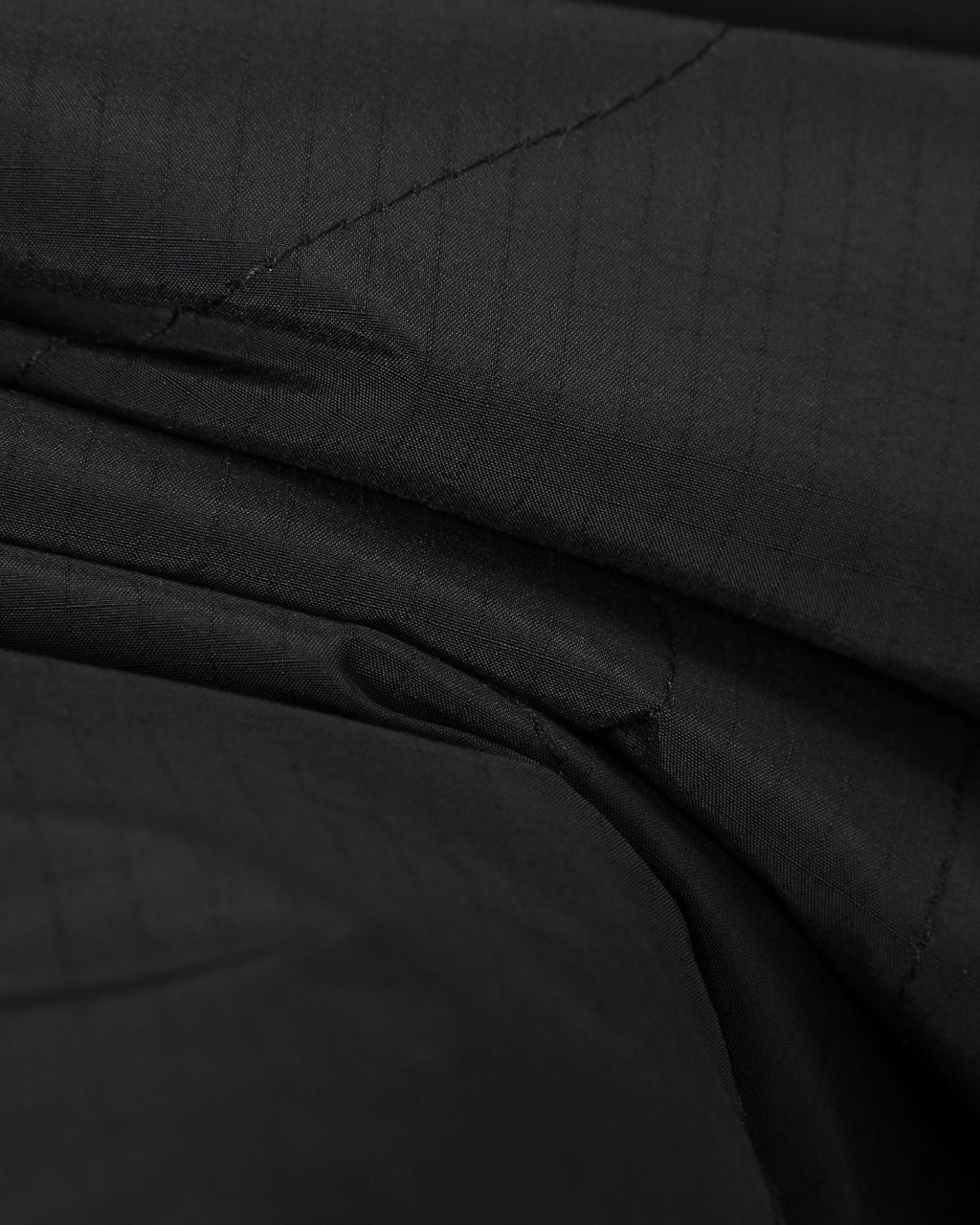 Black quilted fabric close-up with diagonal stitching and layered folds at the seam.