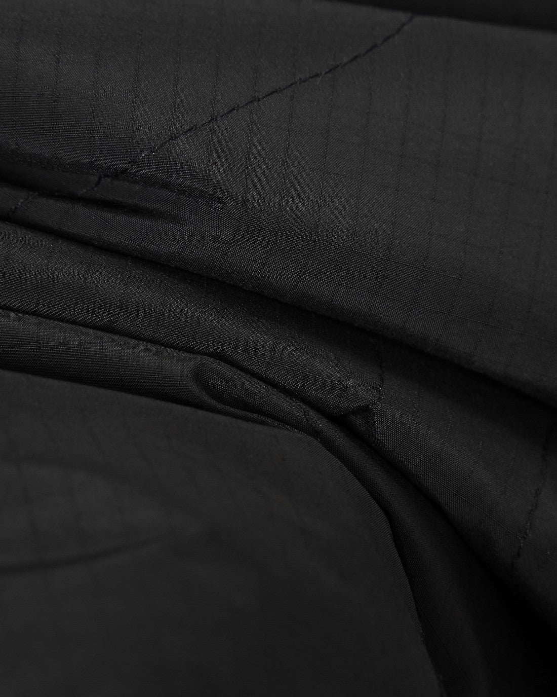 Black quilted fabric close-up with diagonal stitching and layered folds at the seam.