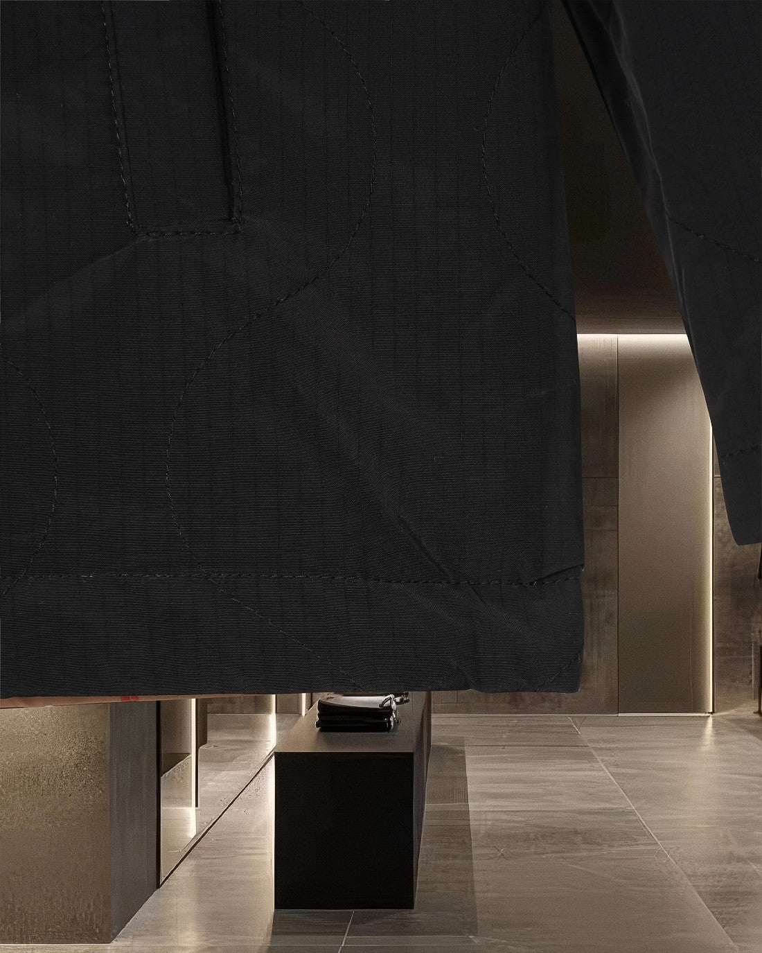 Long black quilted outerwear with stitched panels and button front, front hem visible.