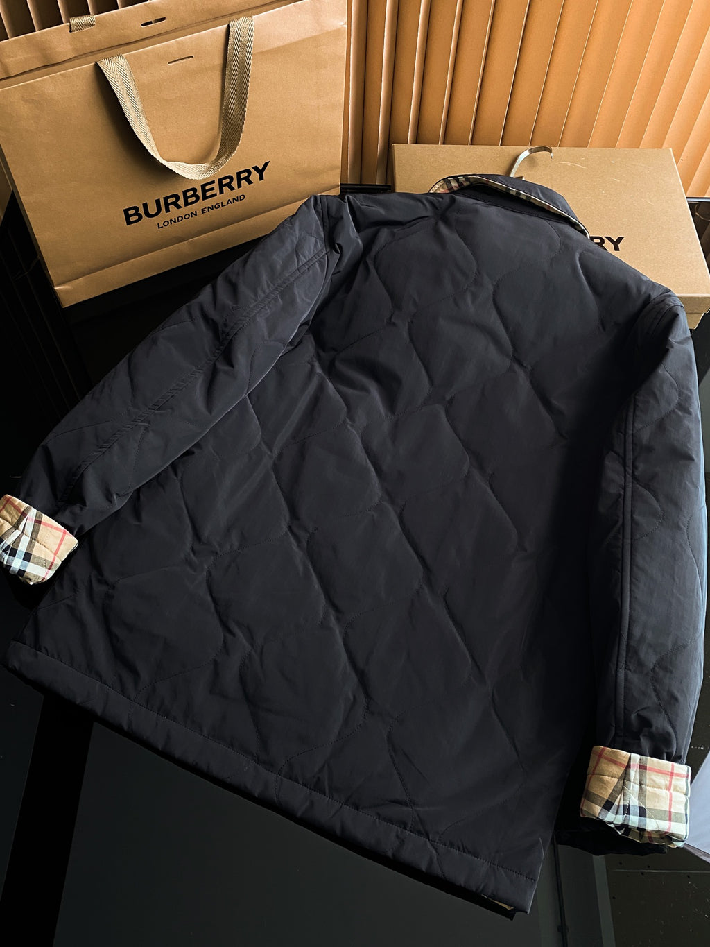 Black quilted long jacket with stand collar and plaid cuff accents