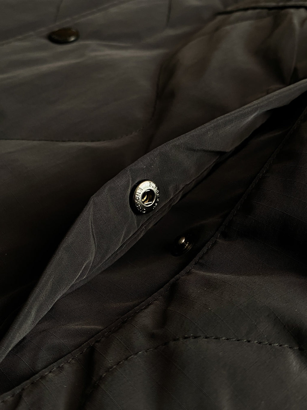 Burberry long coat fabric close-up with dark buttons and stitched pocket detailing.