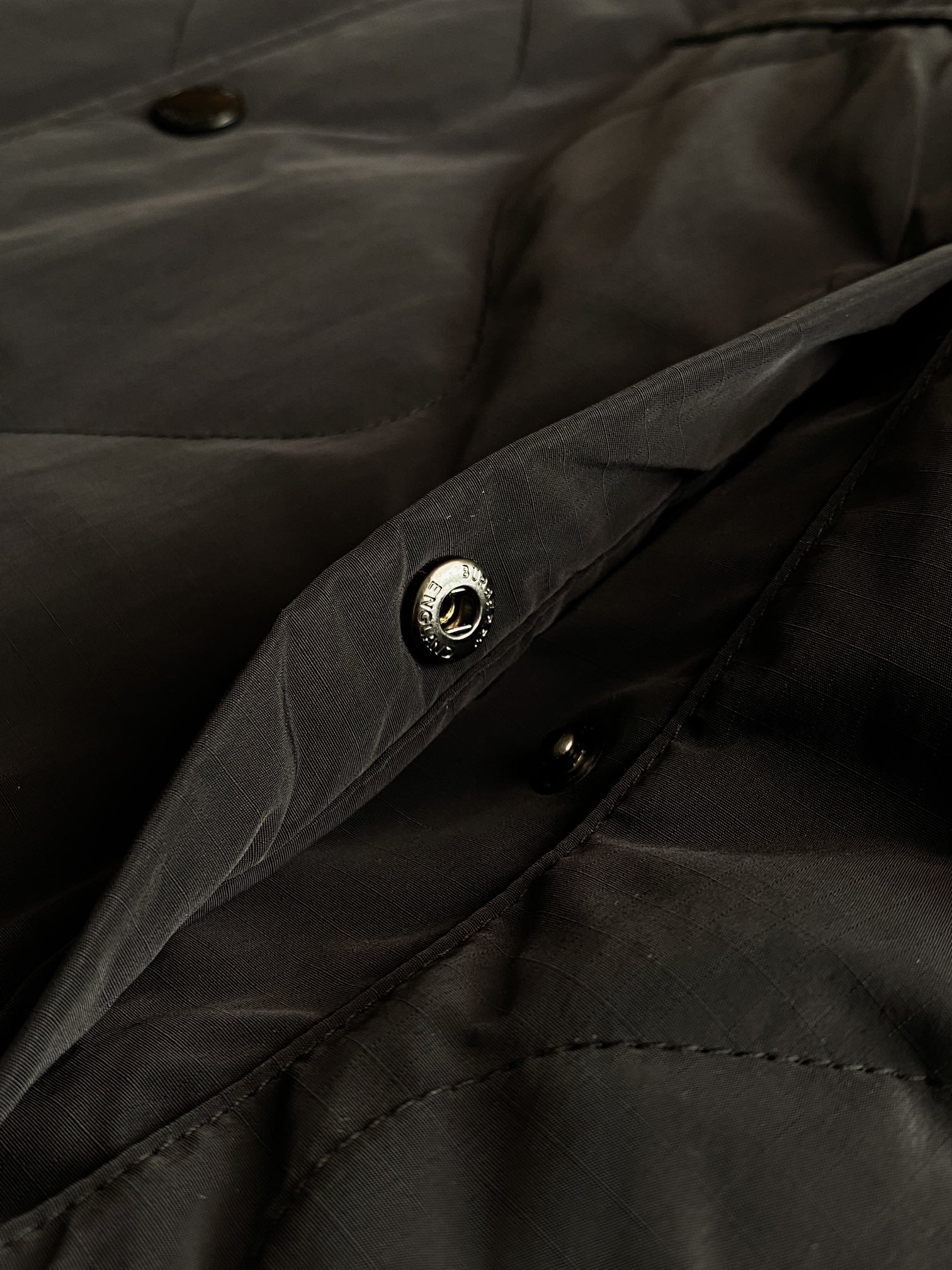 Burberry long coat fabric close-up with dark buttons and stitched pocket detailing.