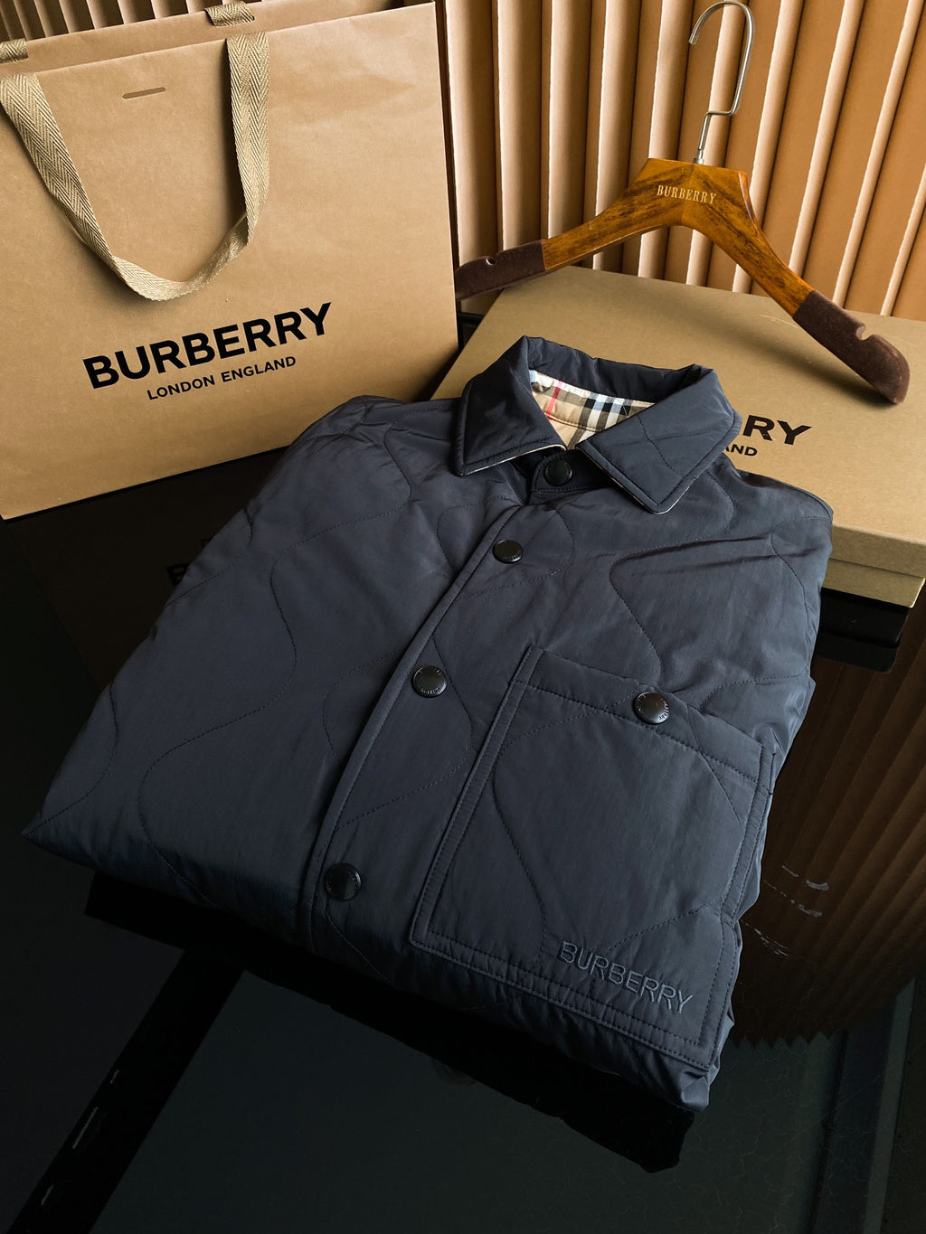 Burberry long quilted coat on hanger, dark color, button front, Burberry logo at hem.