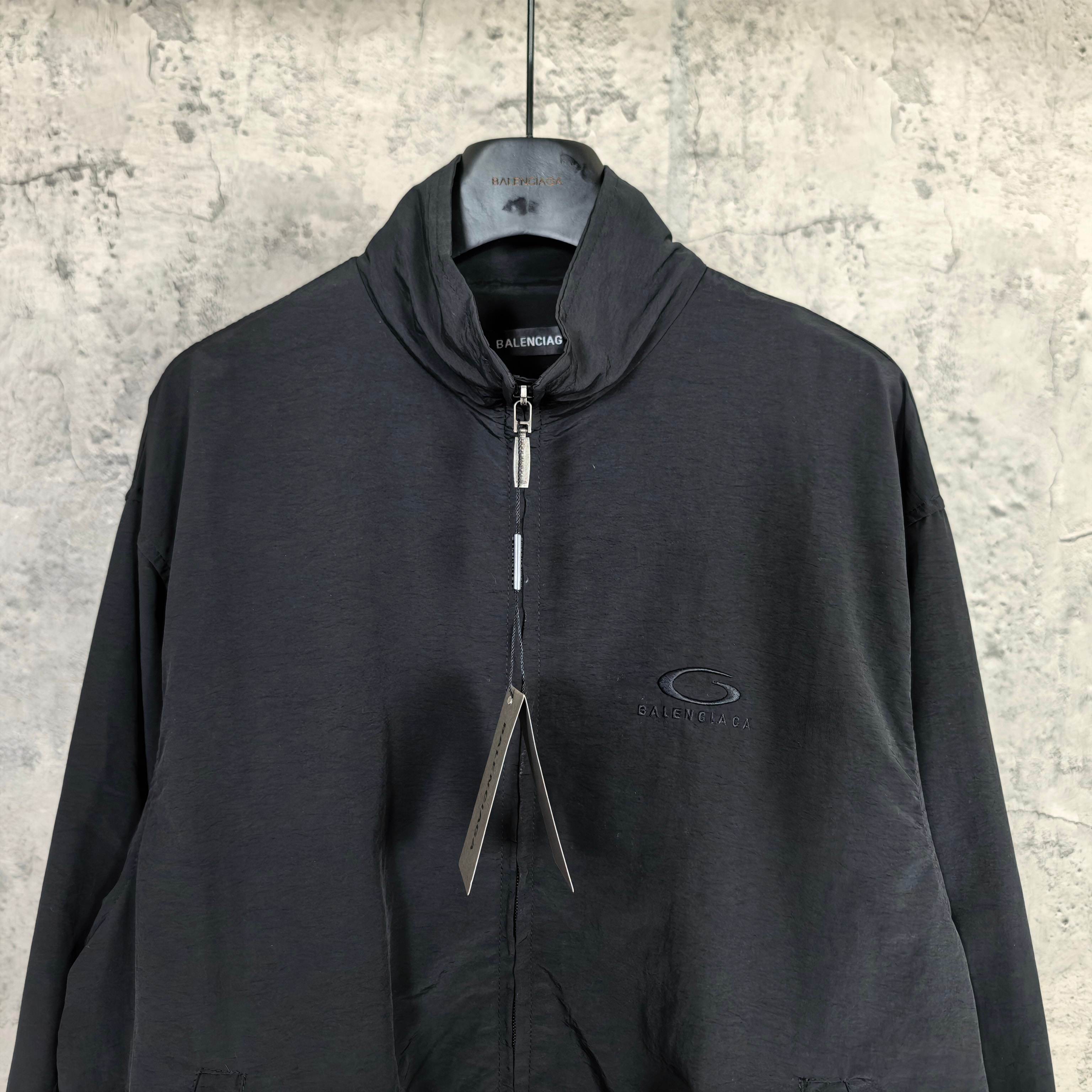 Black Balenciaga zip-up jacket with high collar, drawstrings, and oval chest logo.