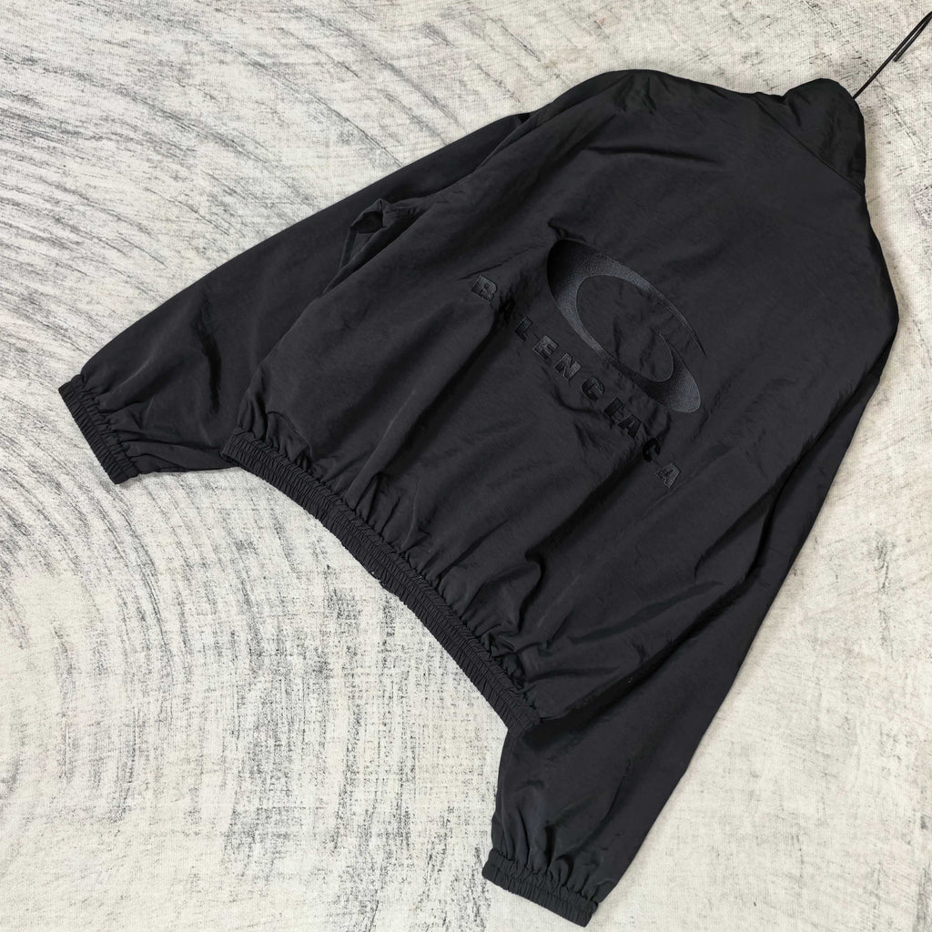 Black Balenciaga zip-up jacket laid flat with back logo graphic and elastic waistband.
