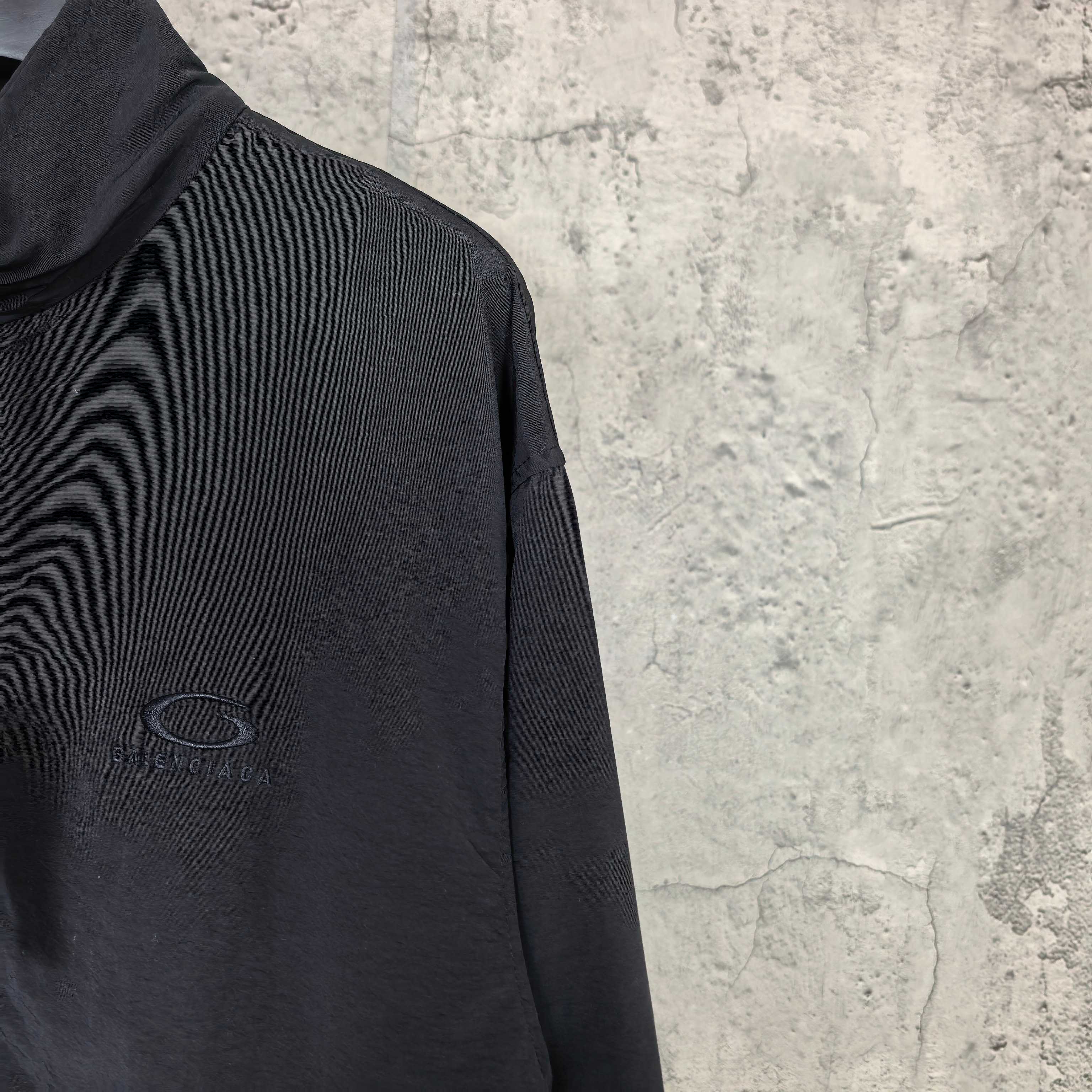 Dark jacket sleeve with small oval logo, zip-up style.