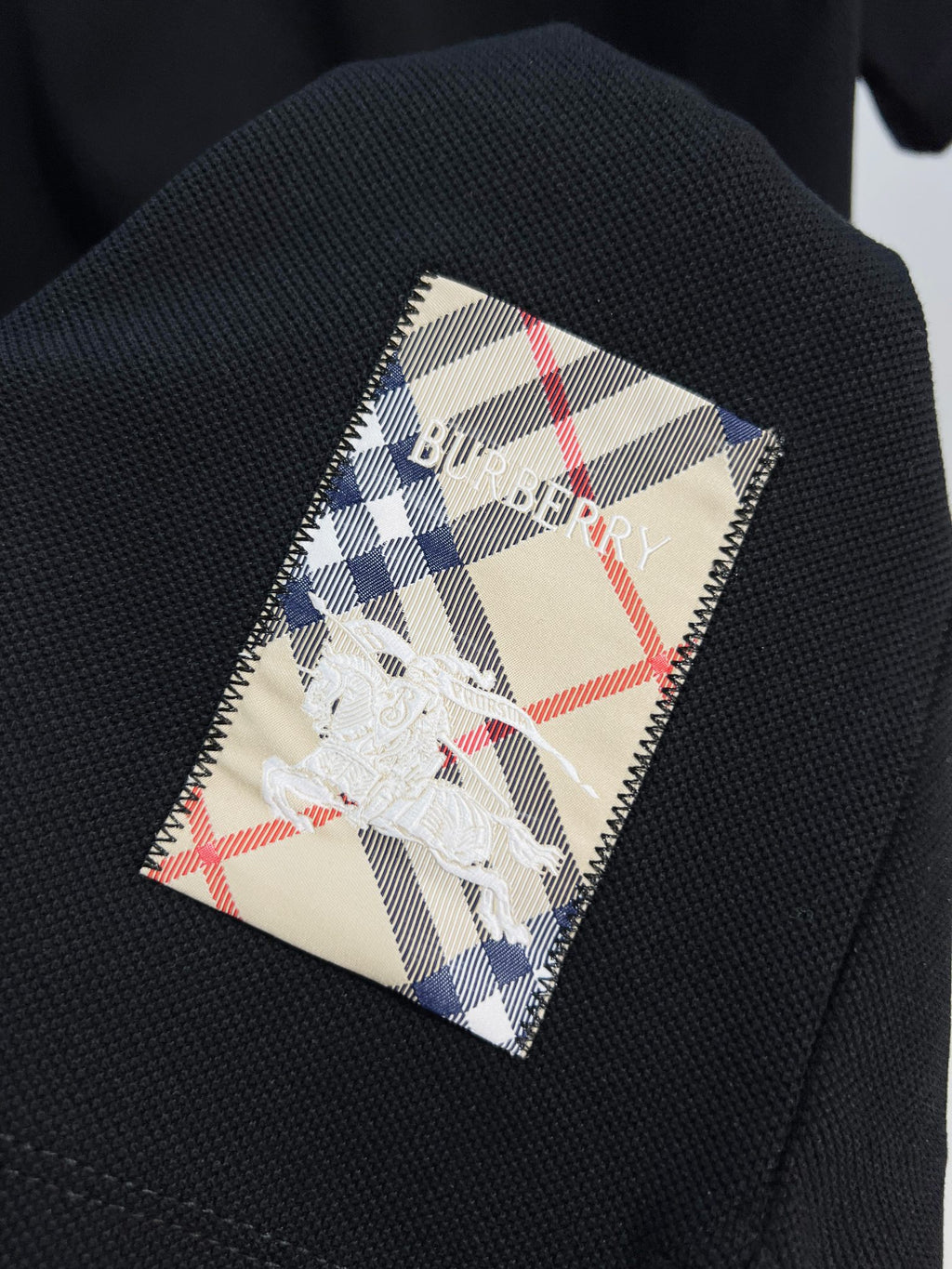 Black polo fabric with plaid inner patch showing blue-and-white horse logo