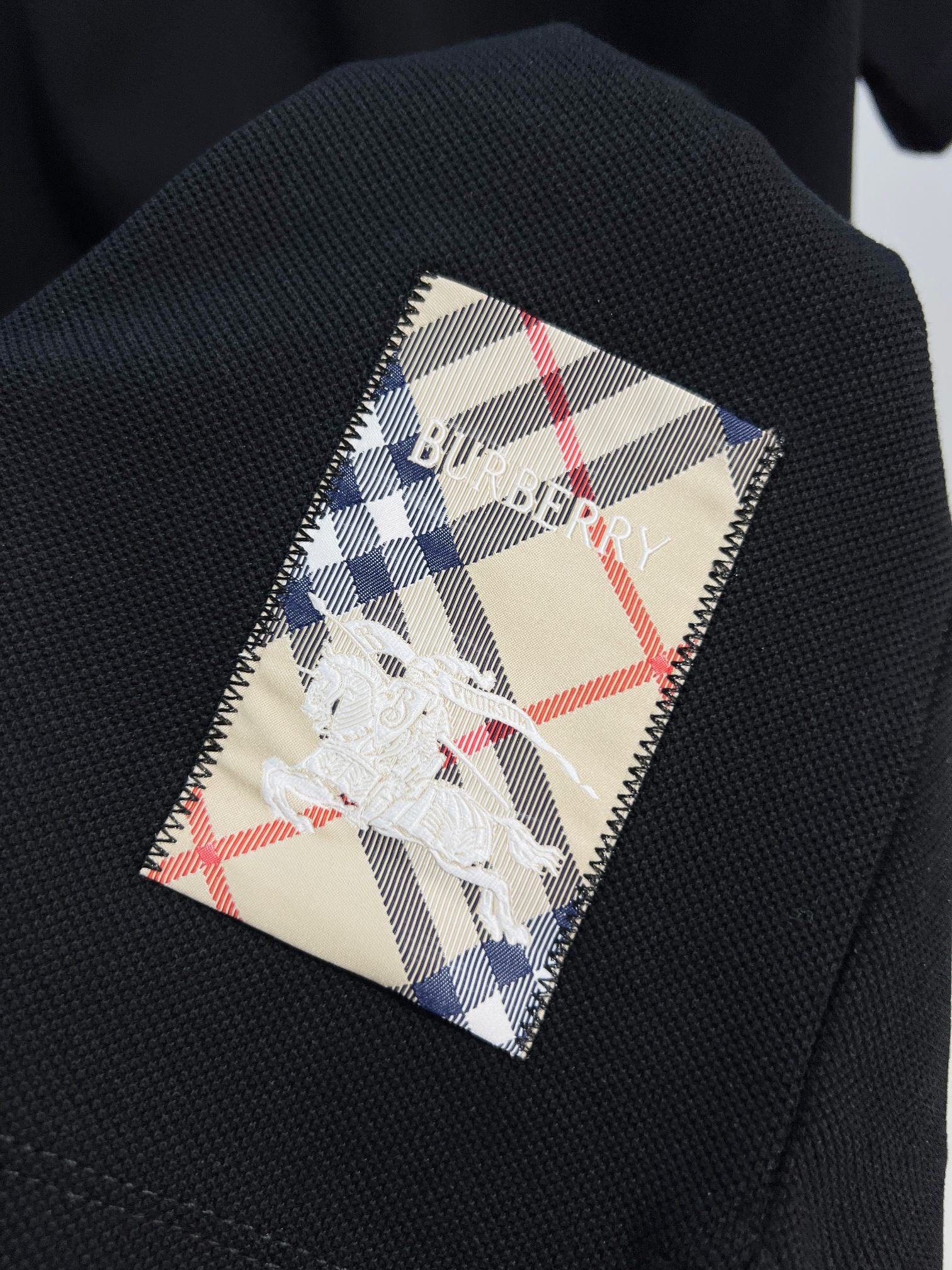 Black polo fabric with plaid inner patch showing blue-and-white horse logo