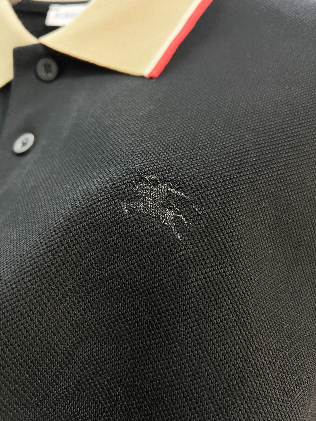 Burberry polo shirt fabric close-up in dark navy with small embroidered logo near chest