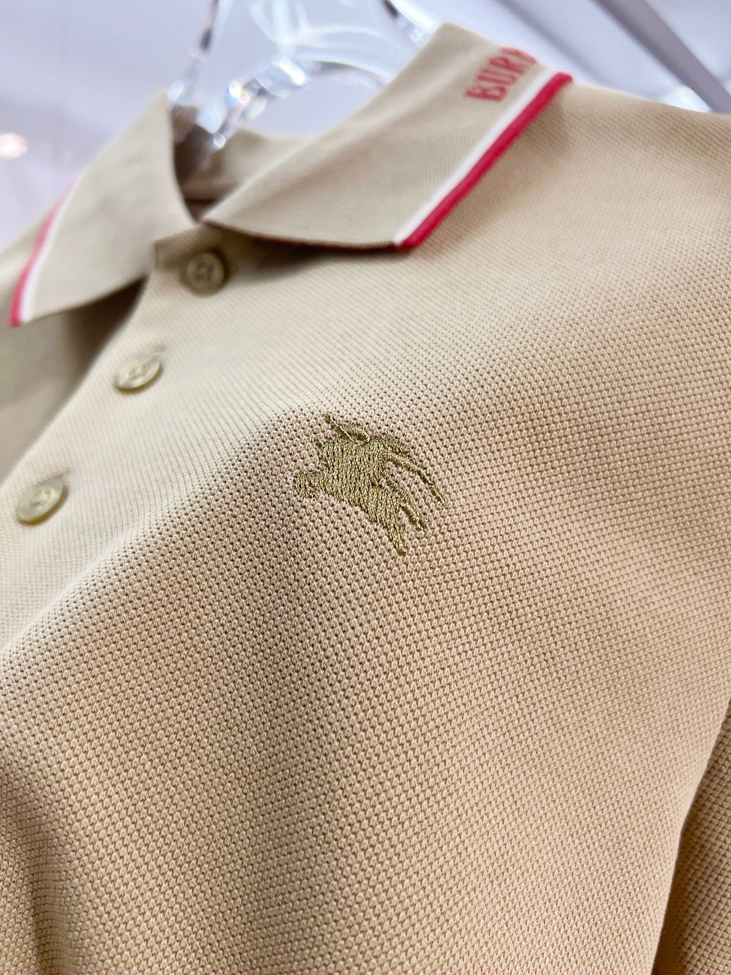 Tan polo shirt close-up of buttons and embroidered horse logo on chest