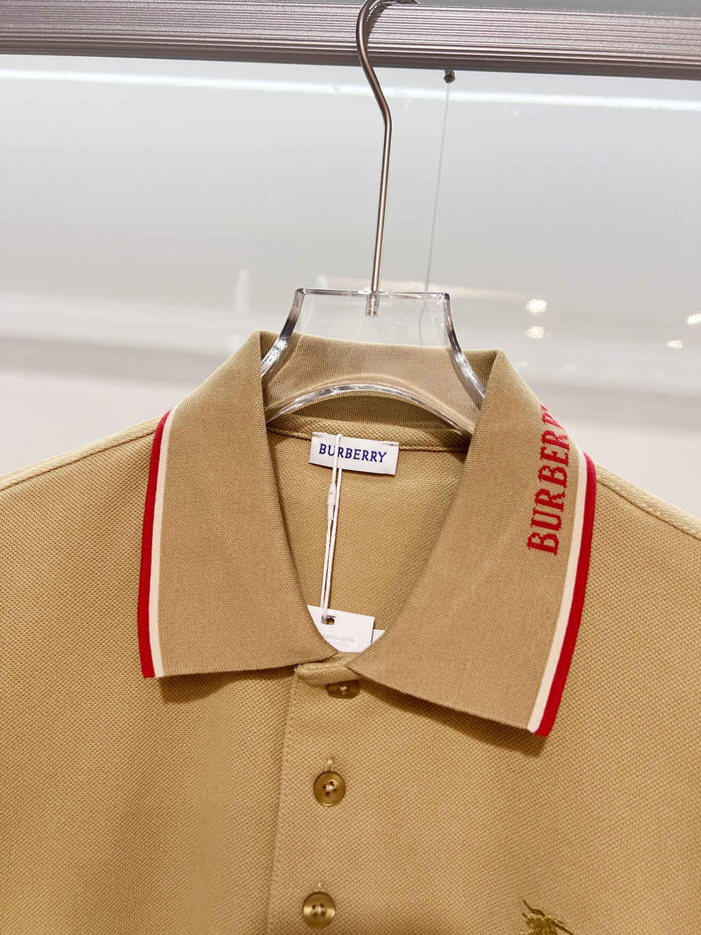 Tan polo shirt front view on hanger with red-trim collar and small horse logo