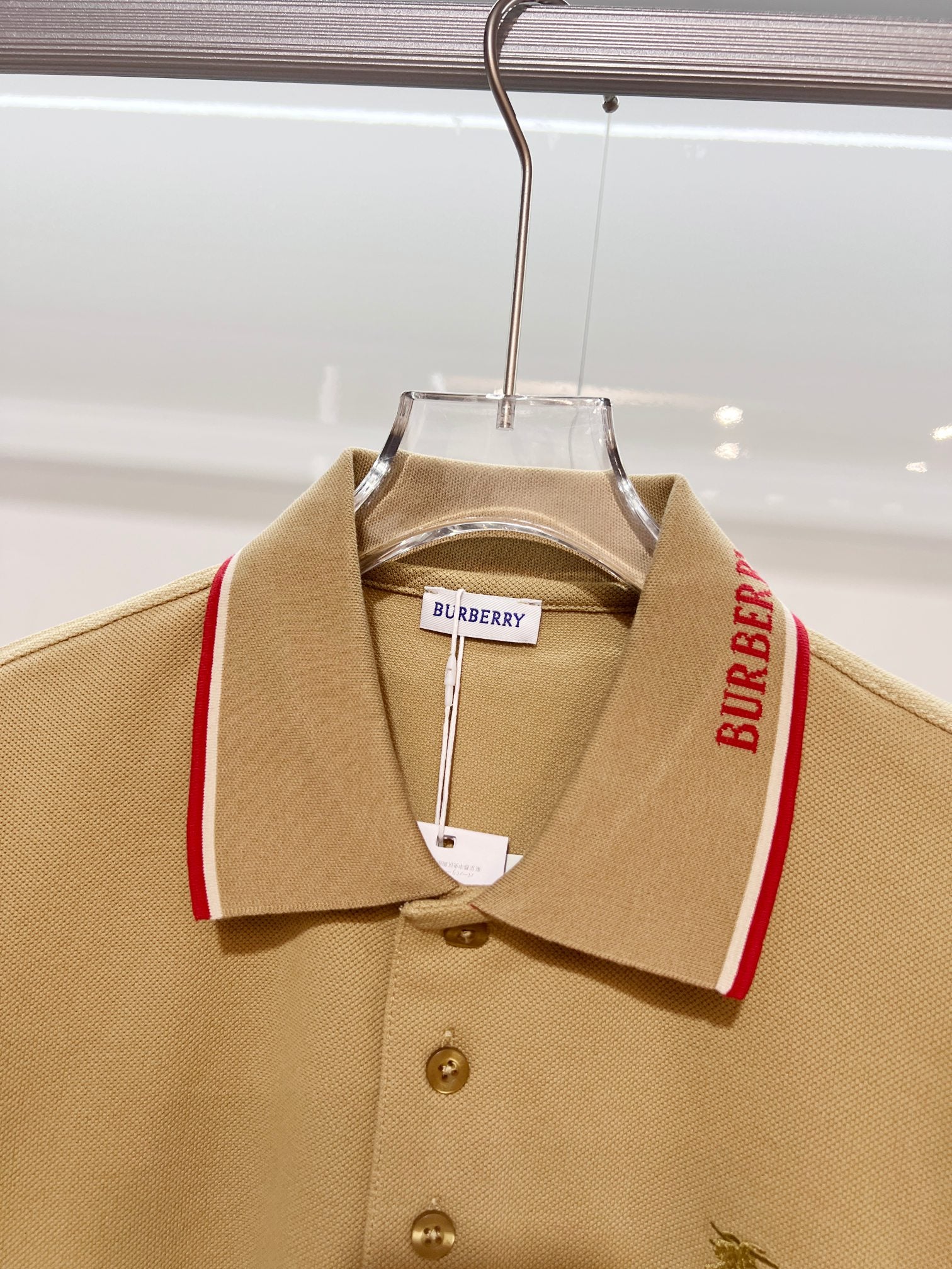 Tan polo shirt front view on hanger with red-trim collar and small horse logo