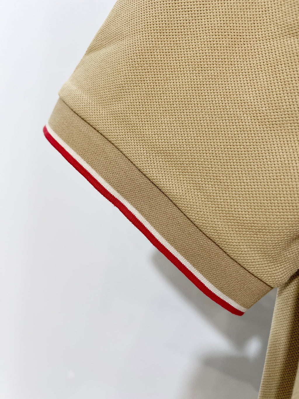 Tan polo shirt sleeve cuff with red-and-white stripe trim
