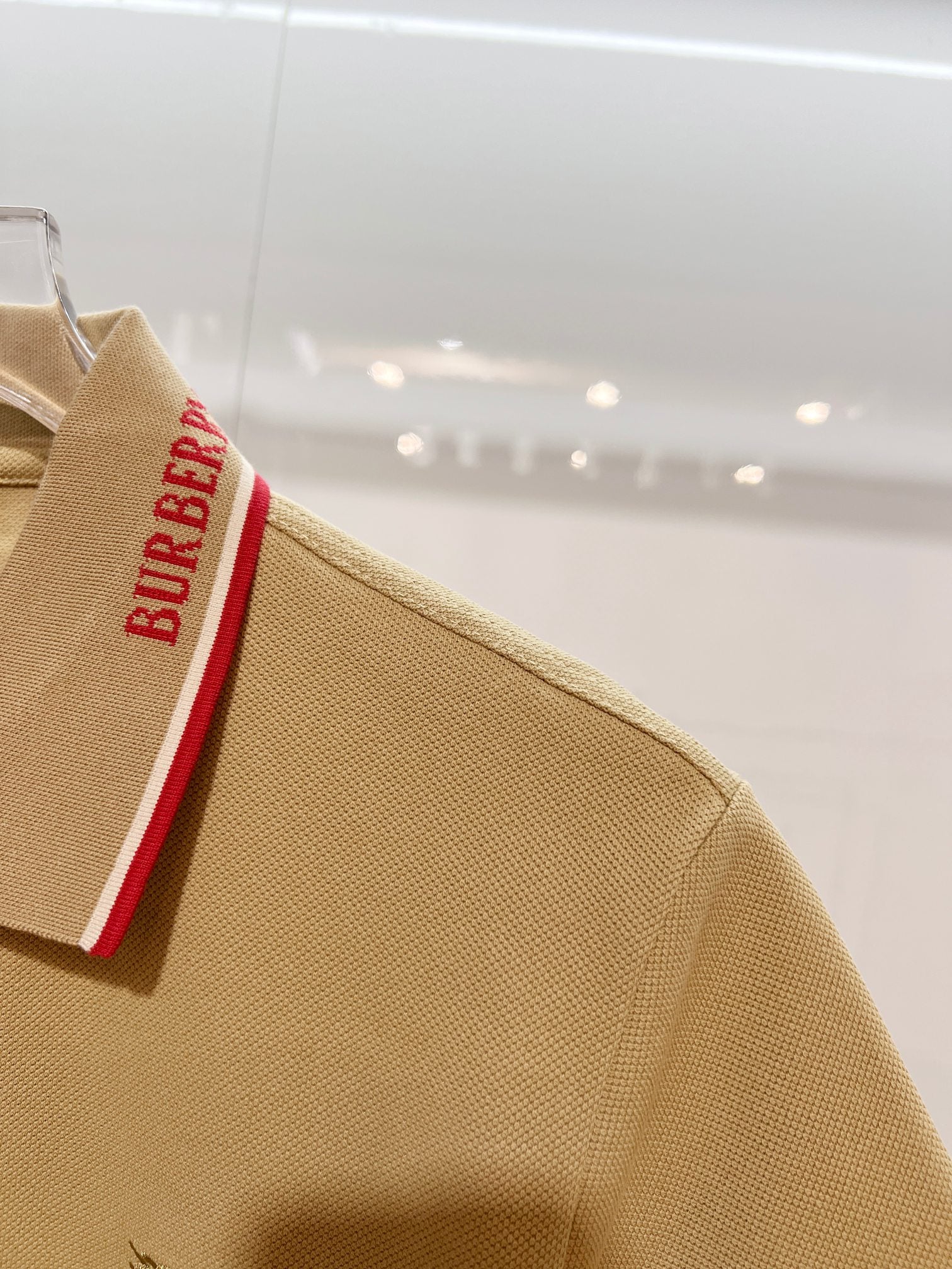 Tan polo shirt with sleeve area and red Burberry trim on collar edge