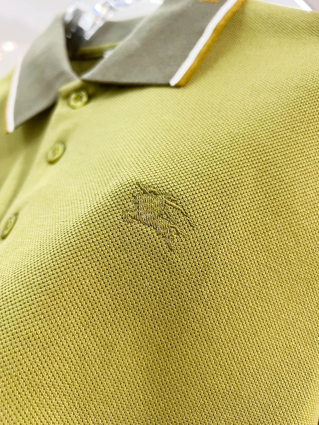Olive green polo fabric with embroidered logo near button placket and cuff trim