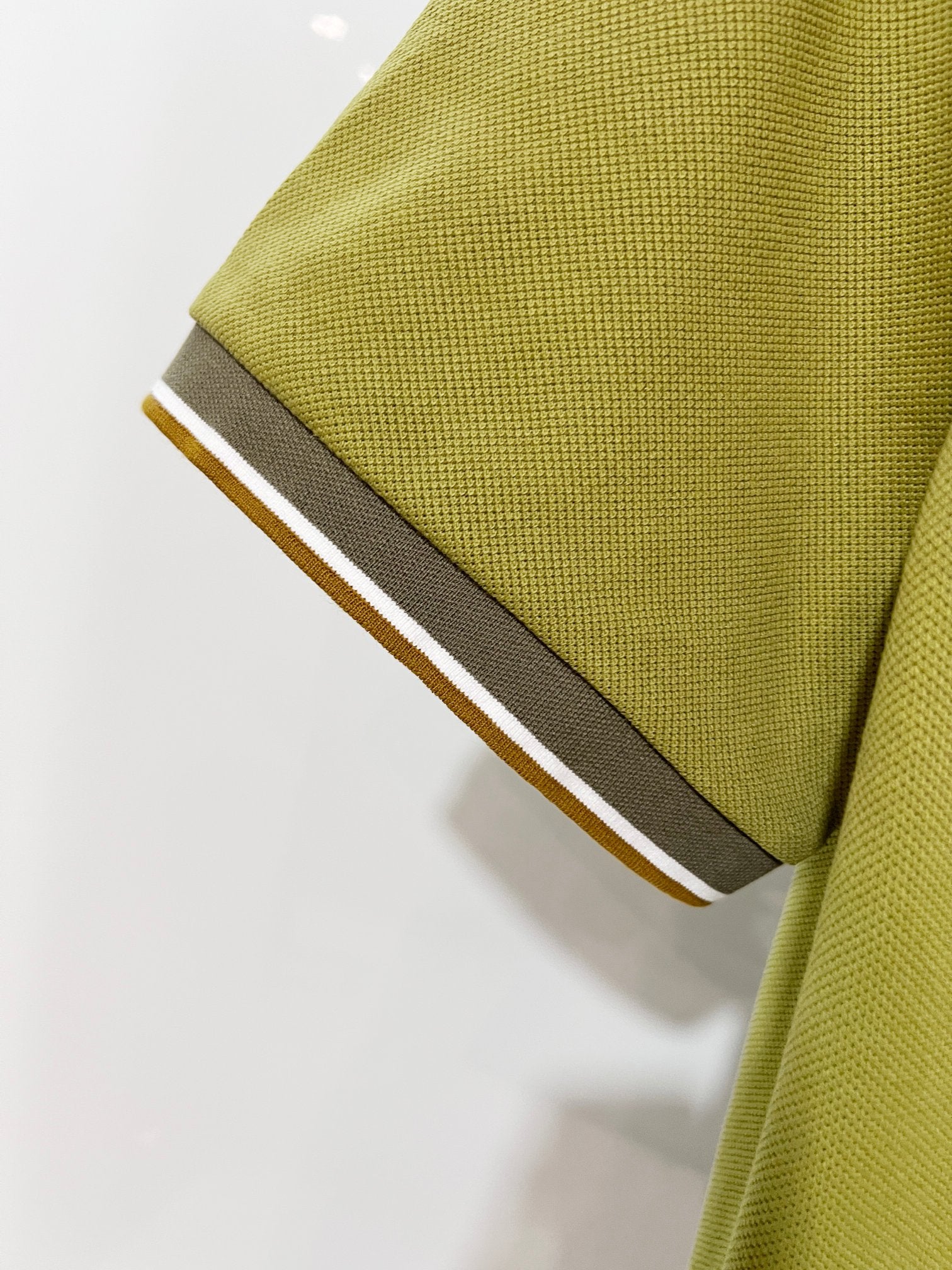 Olive green polo sleeve cuff with contrast dark trim and edge stripe