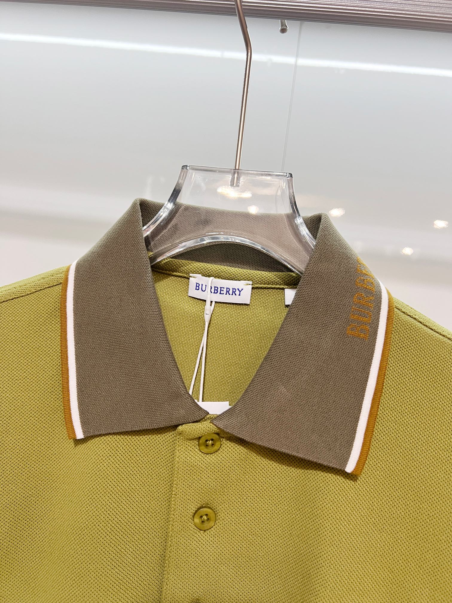 Olive green polo shirt with pointed collar, dark brown placket, and button detail