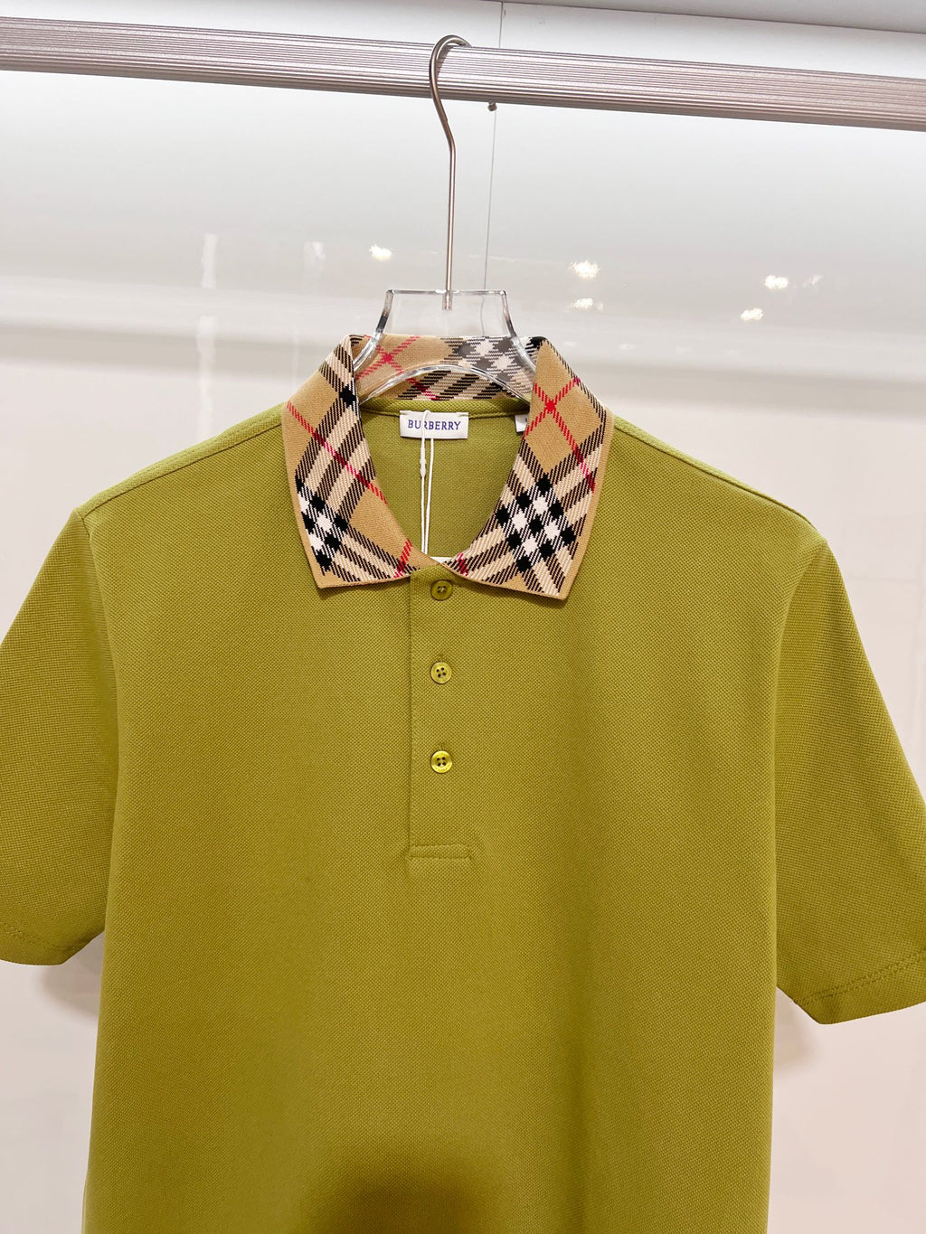 Olive green polo shirt with plaid check collar and buttoned front, close-up