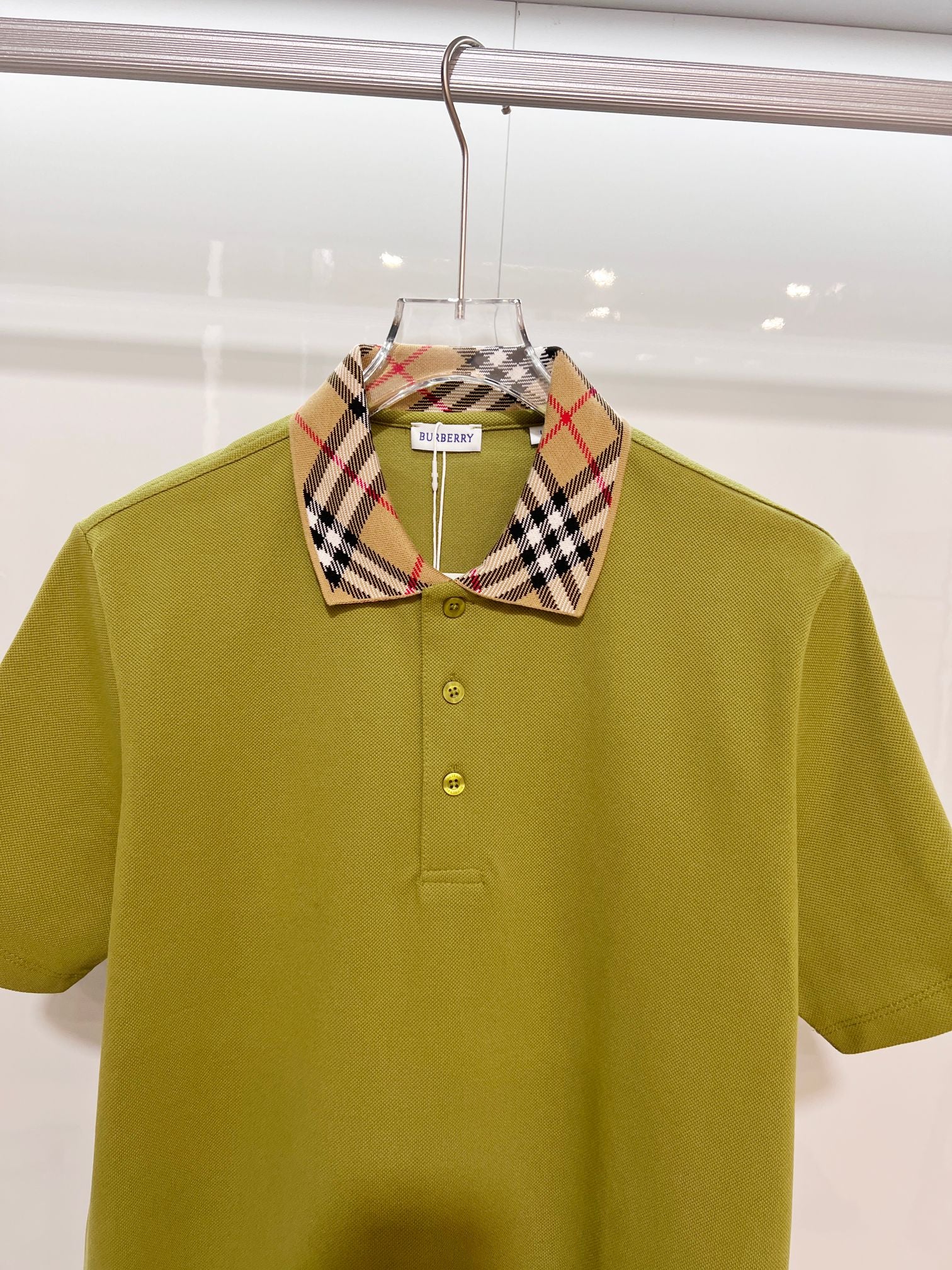 Olive green polo shirt with plaid check collar and buttoned front, close-up