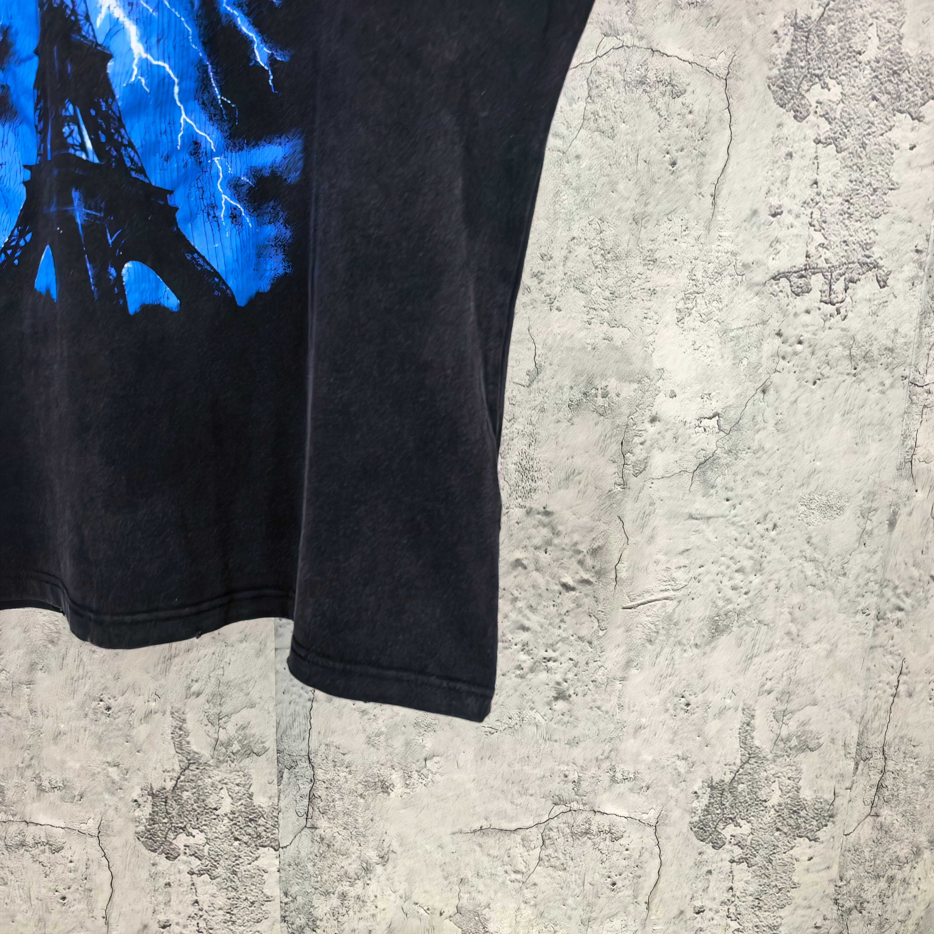 Balenciaga T-shirt hem and side seam detail with blue Eiffel lightning graphic on dark fabric