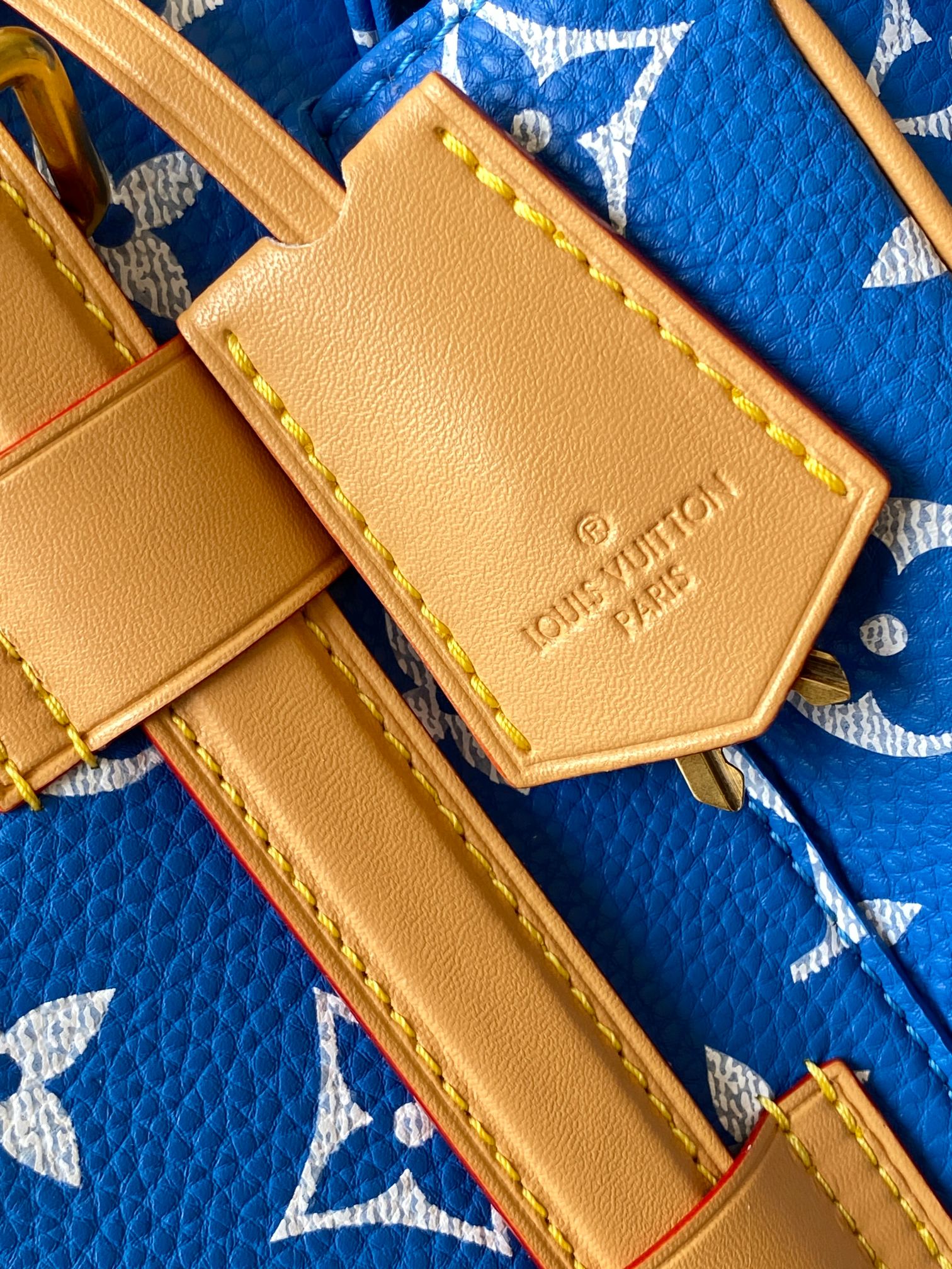 Louis Vuitton leather tab patch with logo and yellow stitching on blue monogram bag