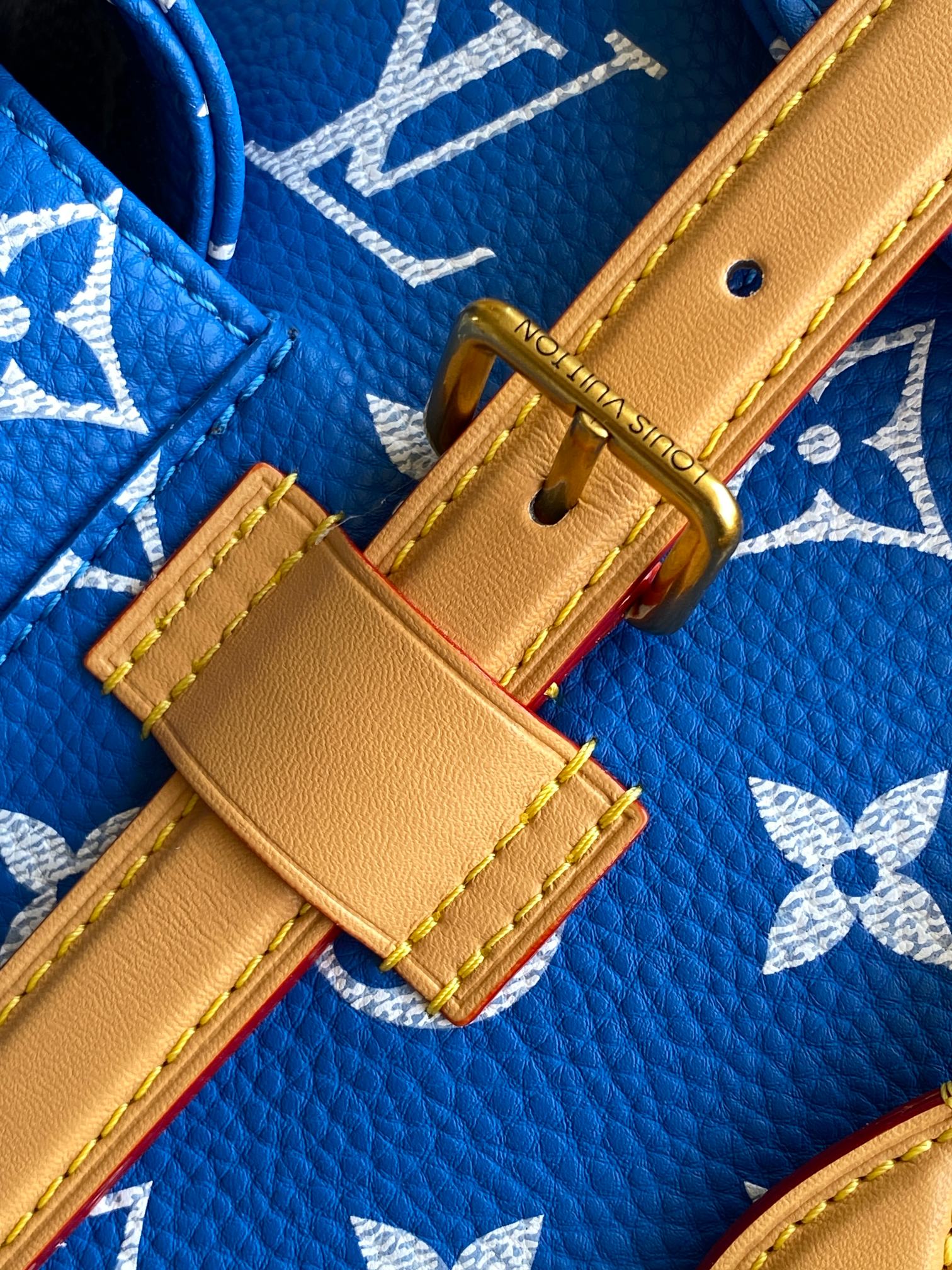 Louis Vuitton blue monogram bag with tan leather strap tab and gold buckle detail