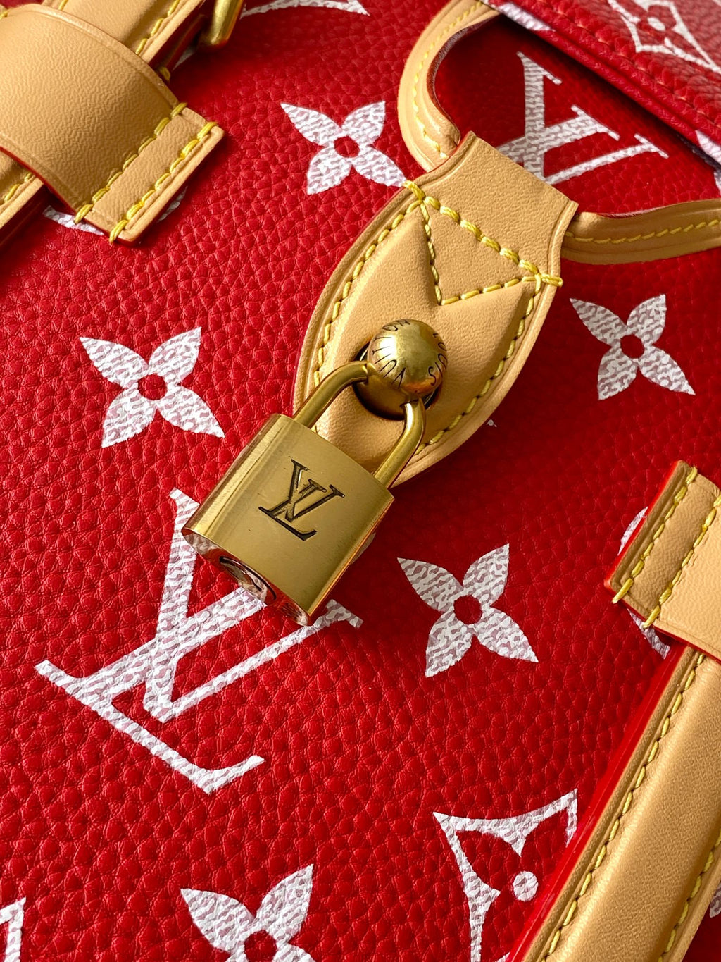 Louis Vuitton red monogram bag close-up with tan leather trim and gold padlock.