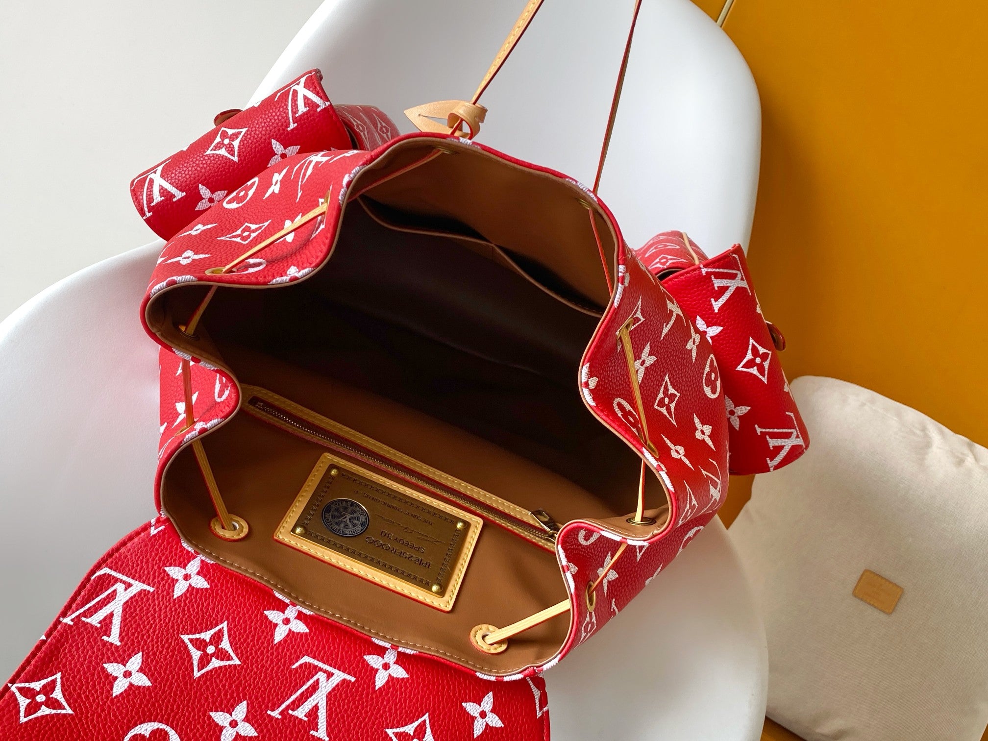Louis Vuitton red monogram bag open to show tan leather interior and gold plaque.