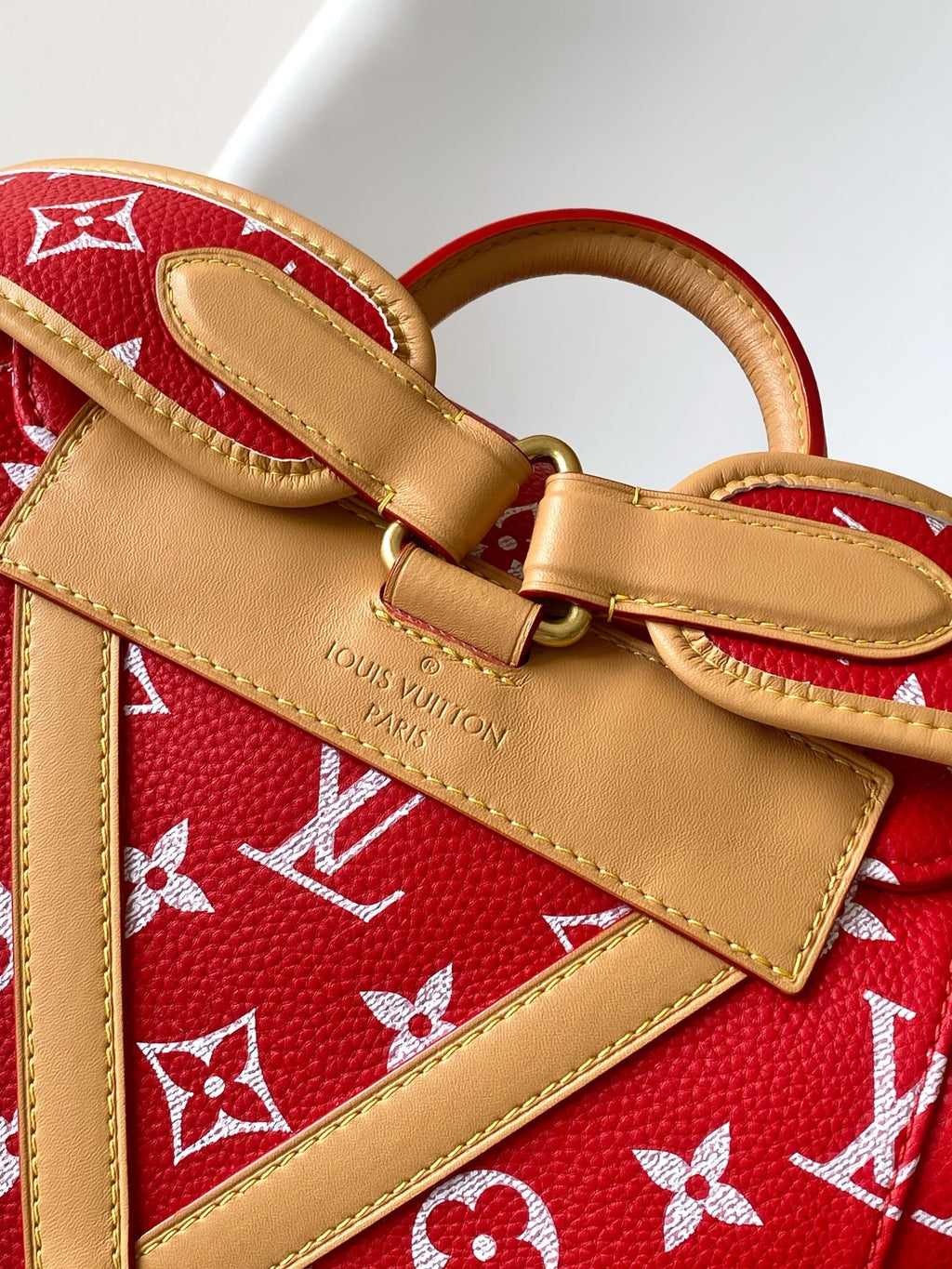 Louis Vuitton red monogram bag with tan leather crossbody strap and brass hardware.