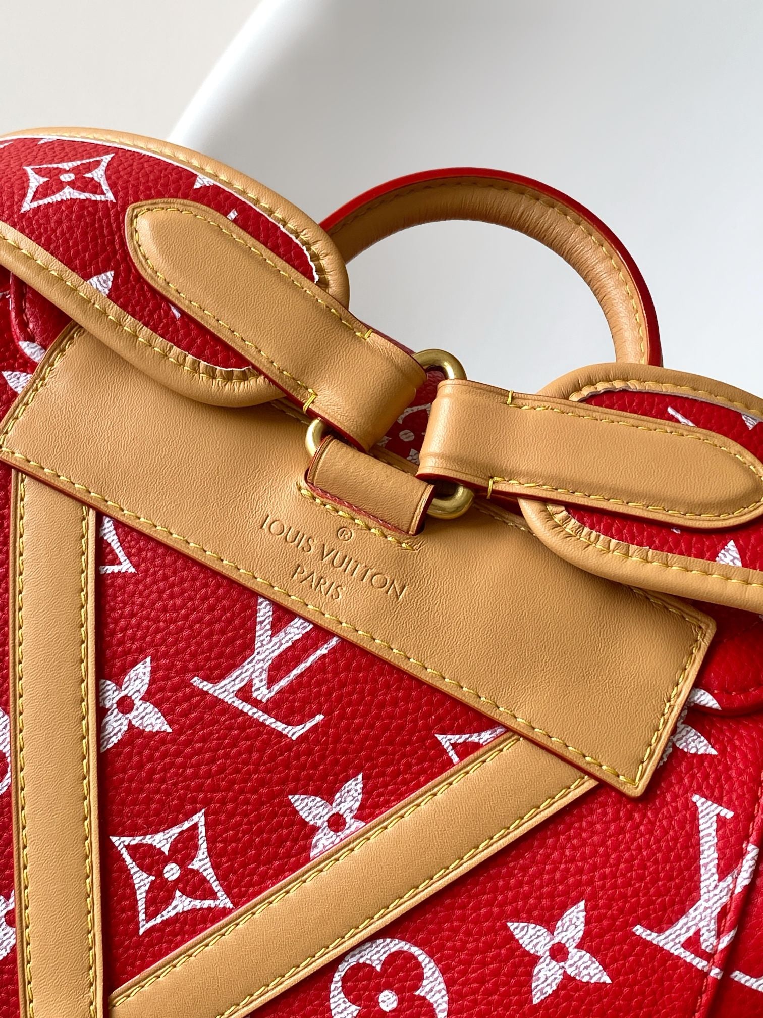 Louis Vuitton red monogram bag with tan leather crossbody strap and brass hardware.