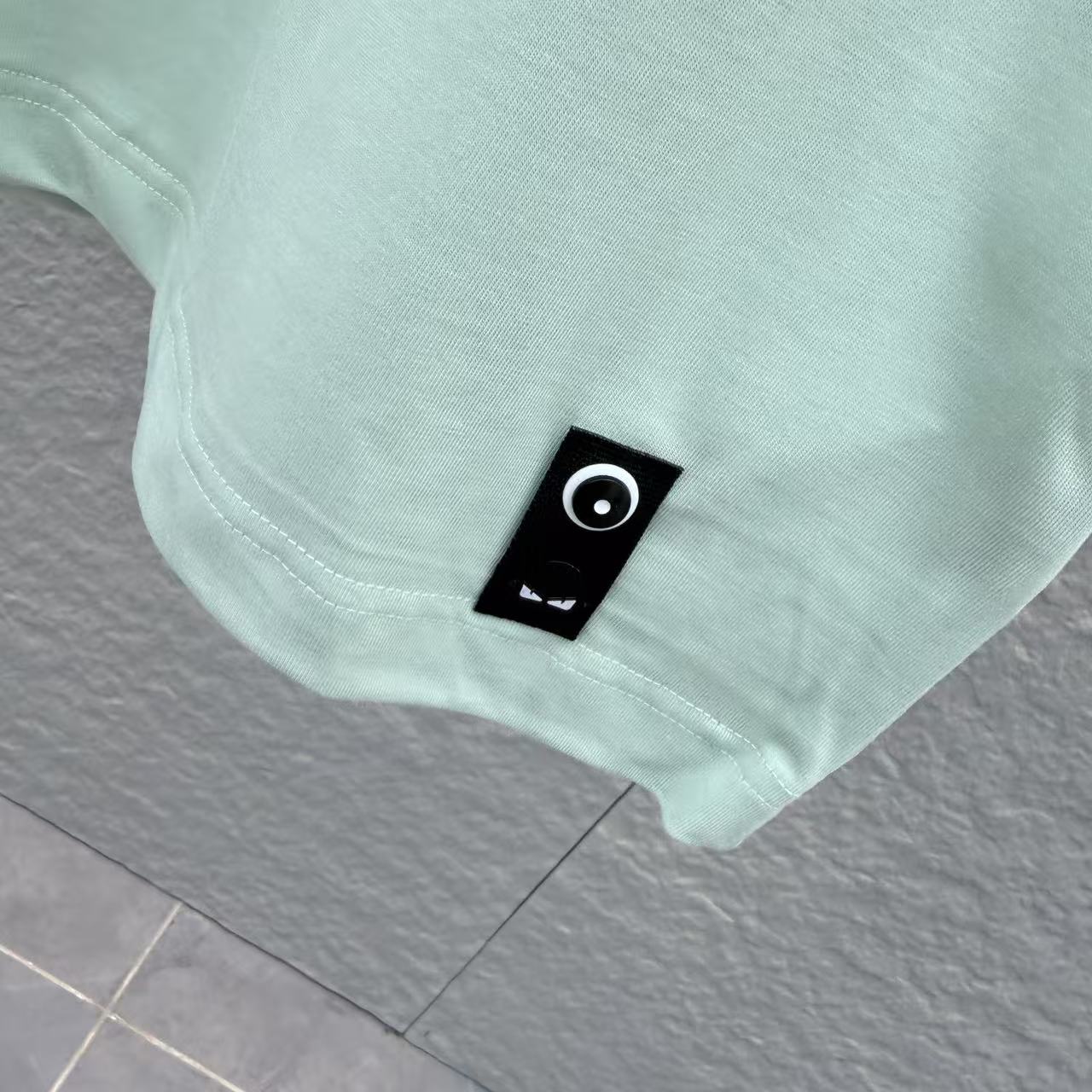 Mint green T-shirt hem with small black brand patch