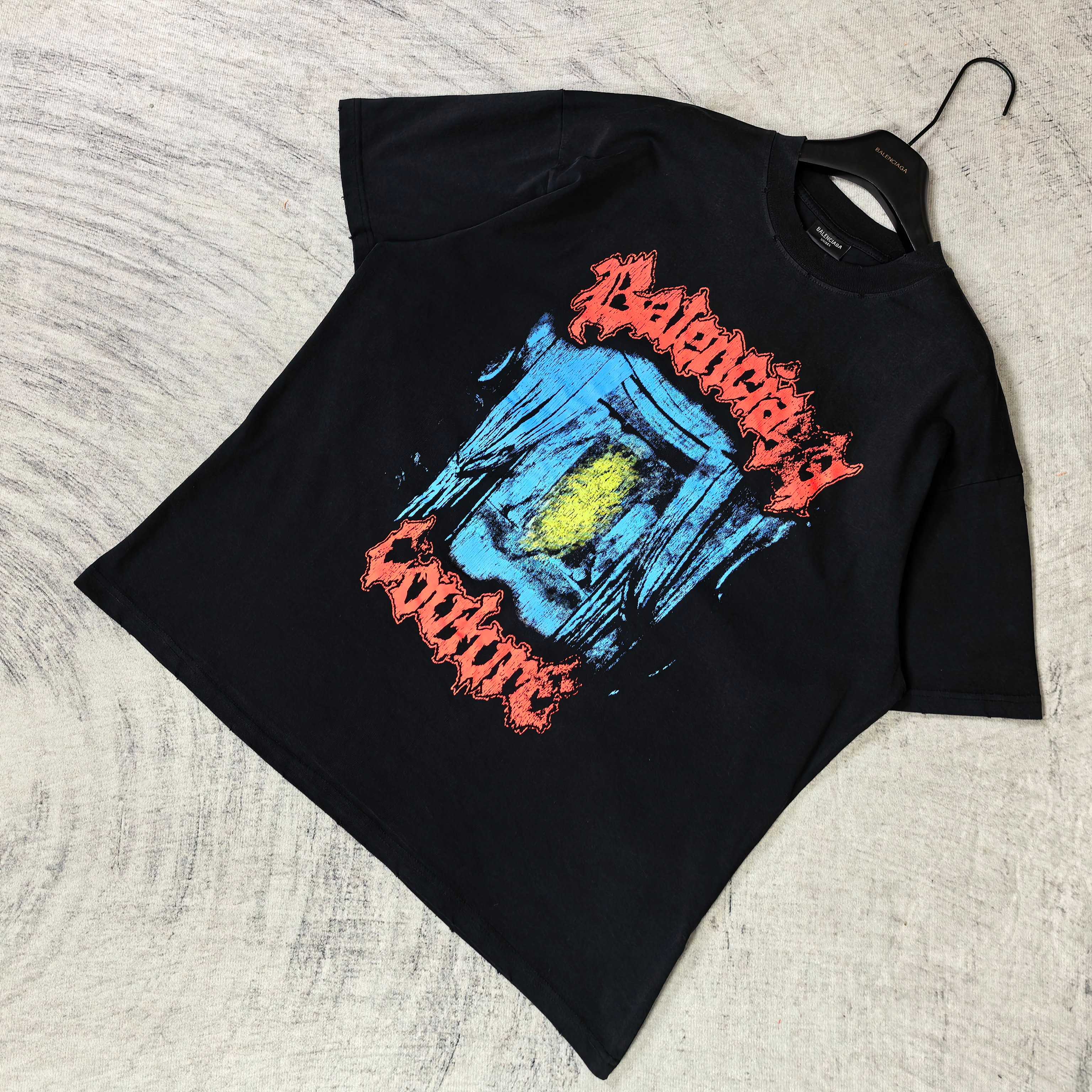 Black T-shirt laid flat with multicolor face graphic and red lettering across chest
