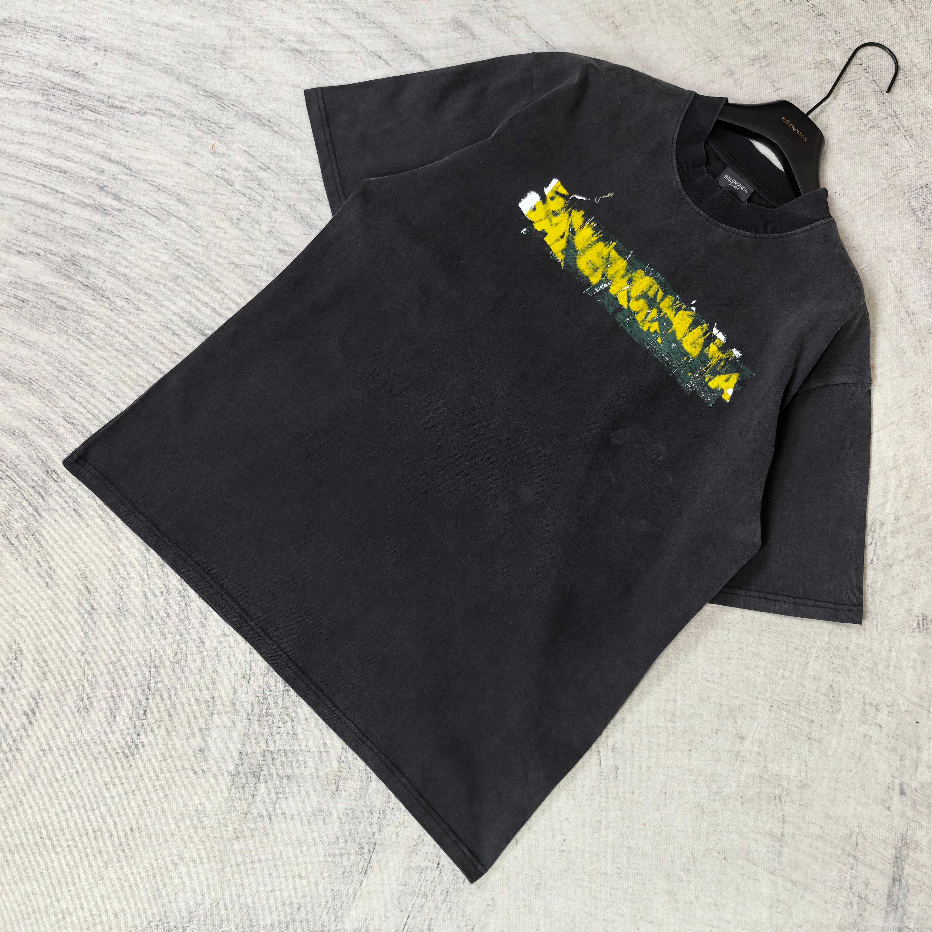 Black short-sleeve T-shirt laid flat with Balenciaga logo graphic on chest.