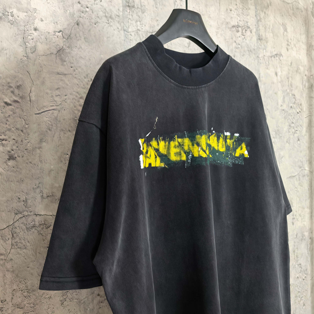 Black short-sleeve T-shirt with Balenciaga logo graphic in yellow and green.
