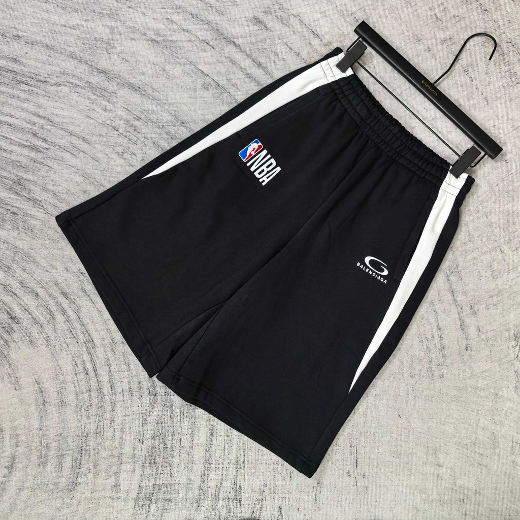 Black shorts with white side stripes, NBA and Balenciaga logos on front, on hanger