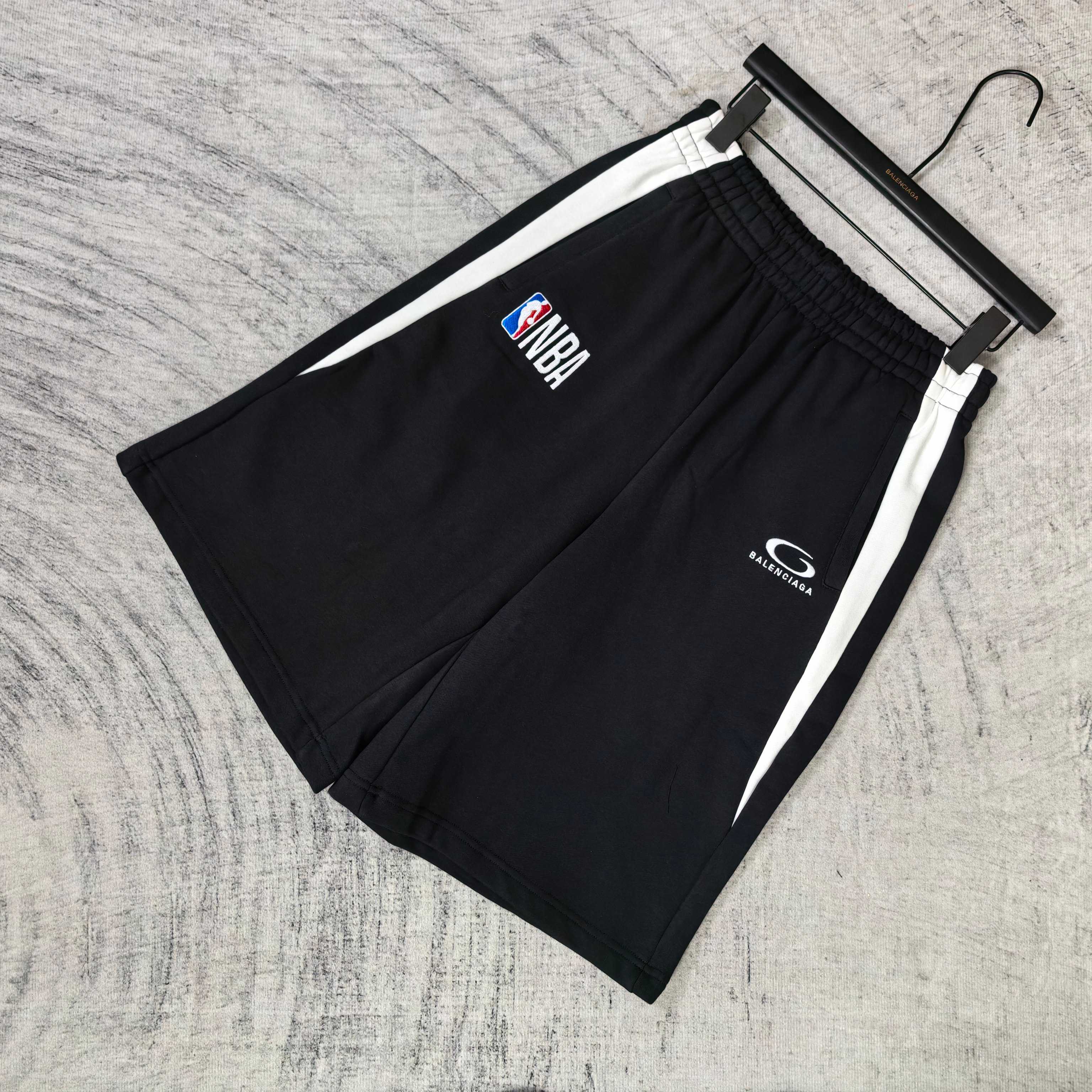 Black shorts with white side stripes, NBA and Balenciaga logos on front, on hanger