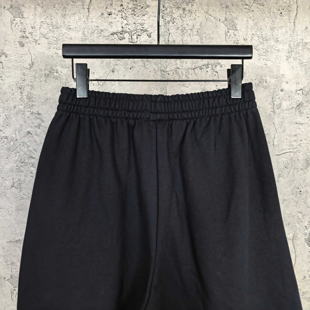 Black shorts with gathered elastic waistband and front pleats, full view on hanger