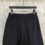Black shorts with gathered elastic waistband and front pleats, full view on hanger