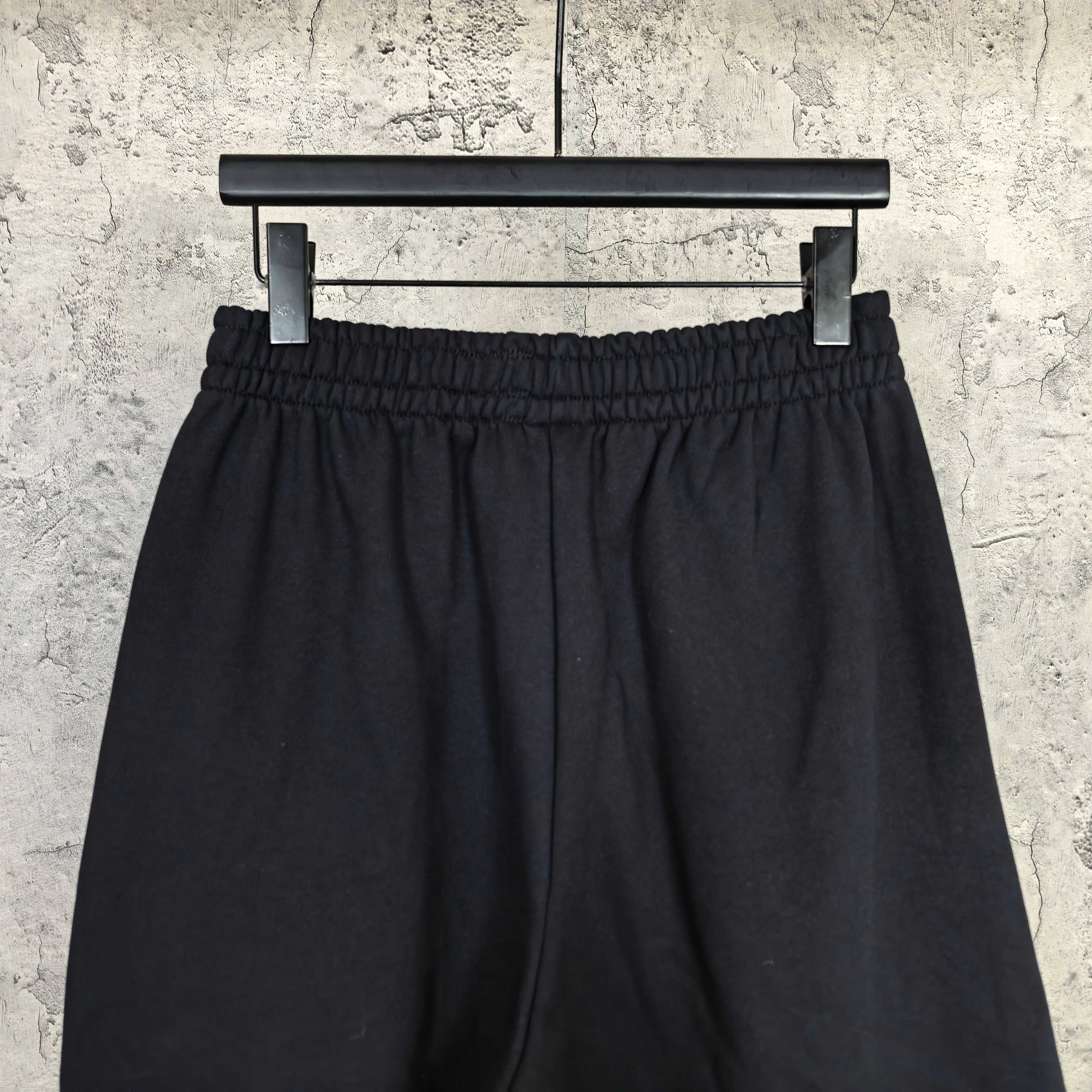 Black shorts with gathered elastic waistband and front pleats, full view on hanger
