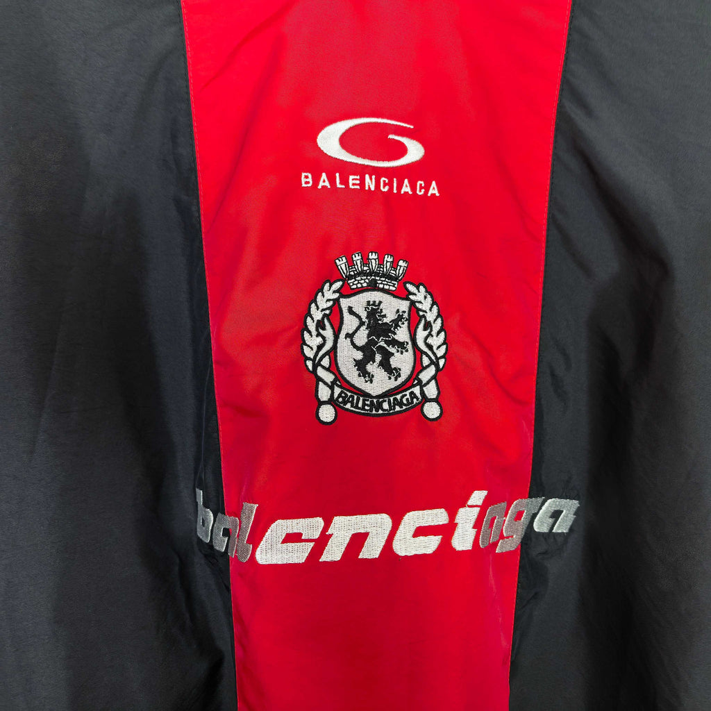 Balenciaga jersey front close-up: white logo, crest emblem, and lower stylized text.