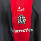 Balenciaga jersey front close-up: white logo, crest emblem, and lower stylized text.