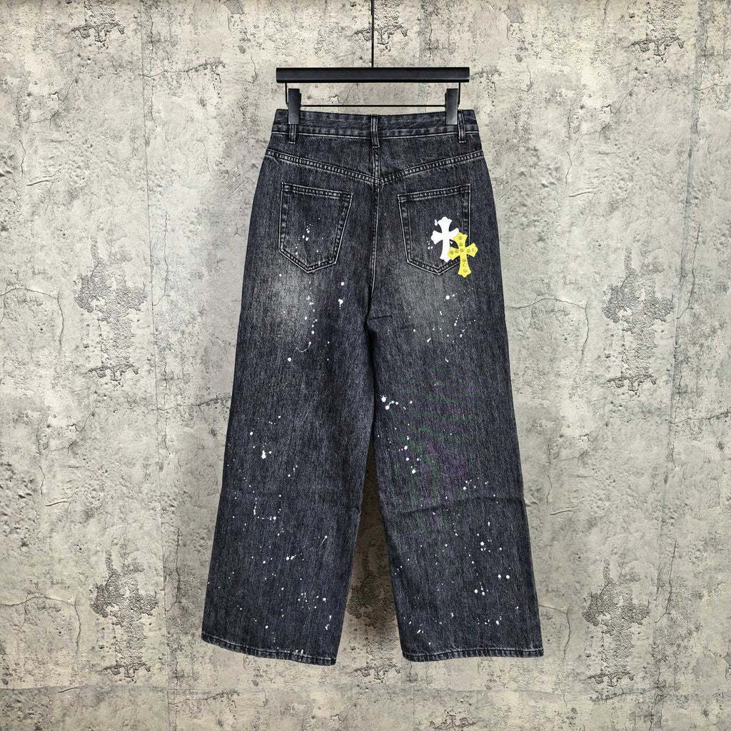 Dark denim pants with speckled finish and small white graphic cross on thigh